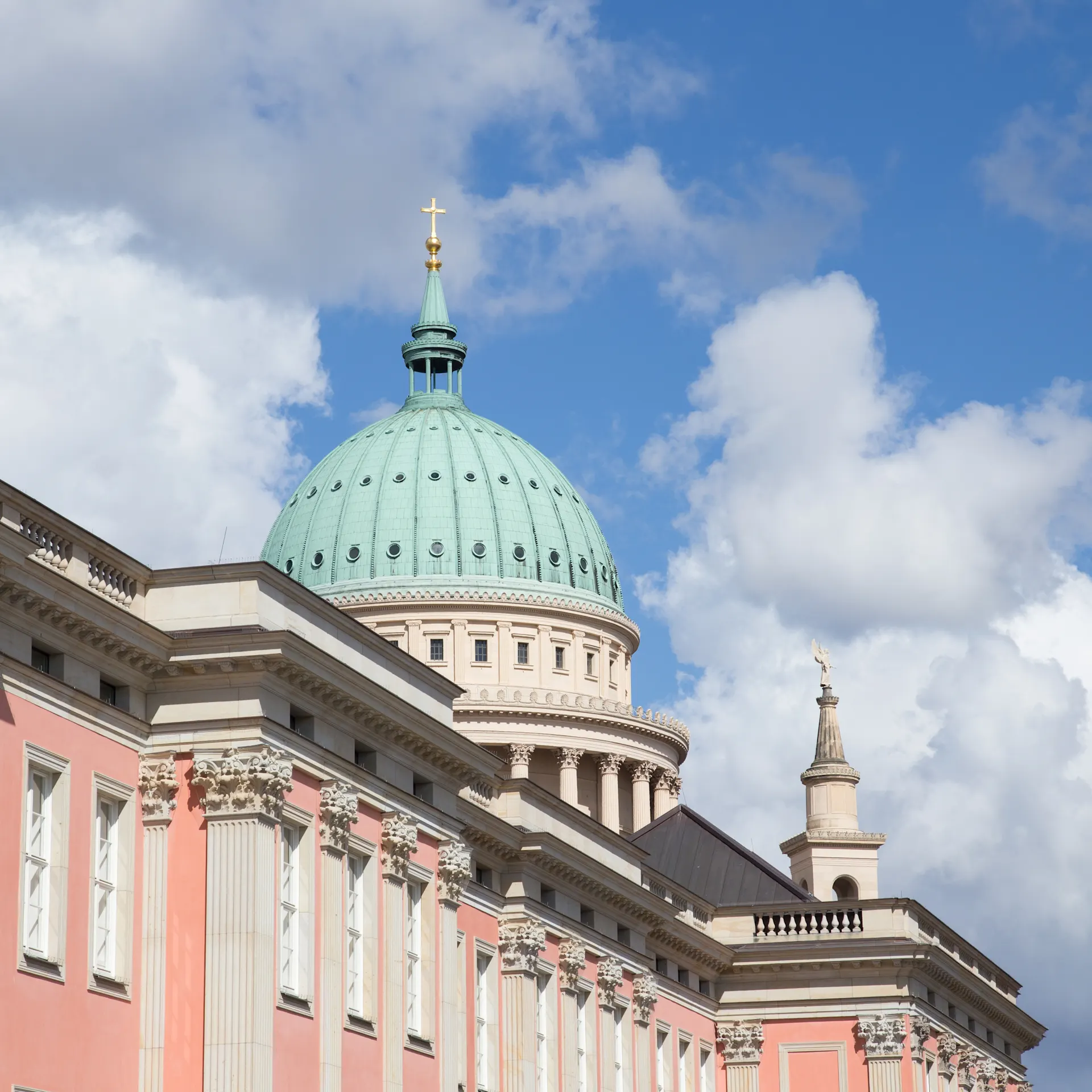 Großes Gebäude mit rosa Fassade und grüner Kuppel vor blauem Himmel.