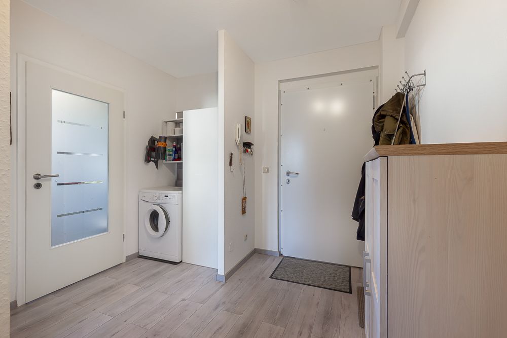 Flur mit Waschmaschine, Garderobe, Schuhschrank und weißer Eingangstür.