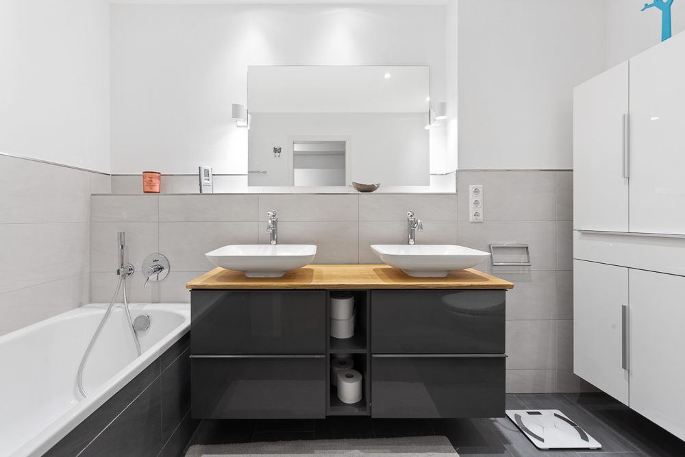 Modernes Badezimmer mit zwei Waschbecken, Spiegel, Badewanne und weißen Schränken.