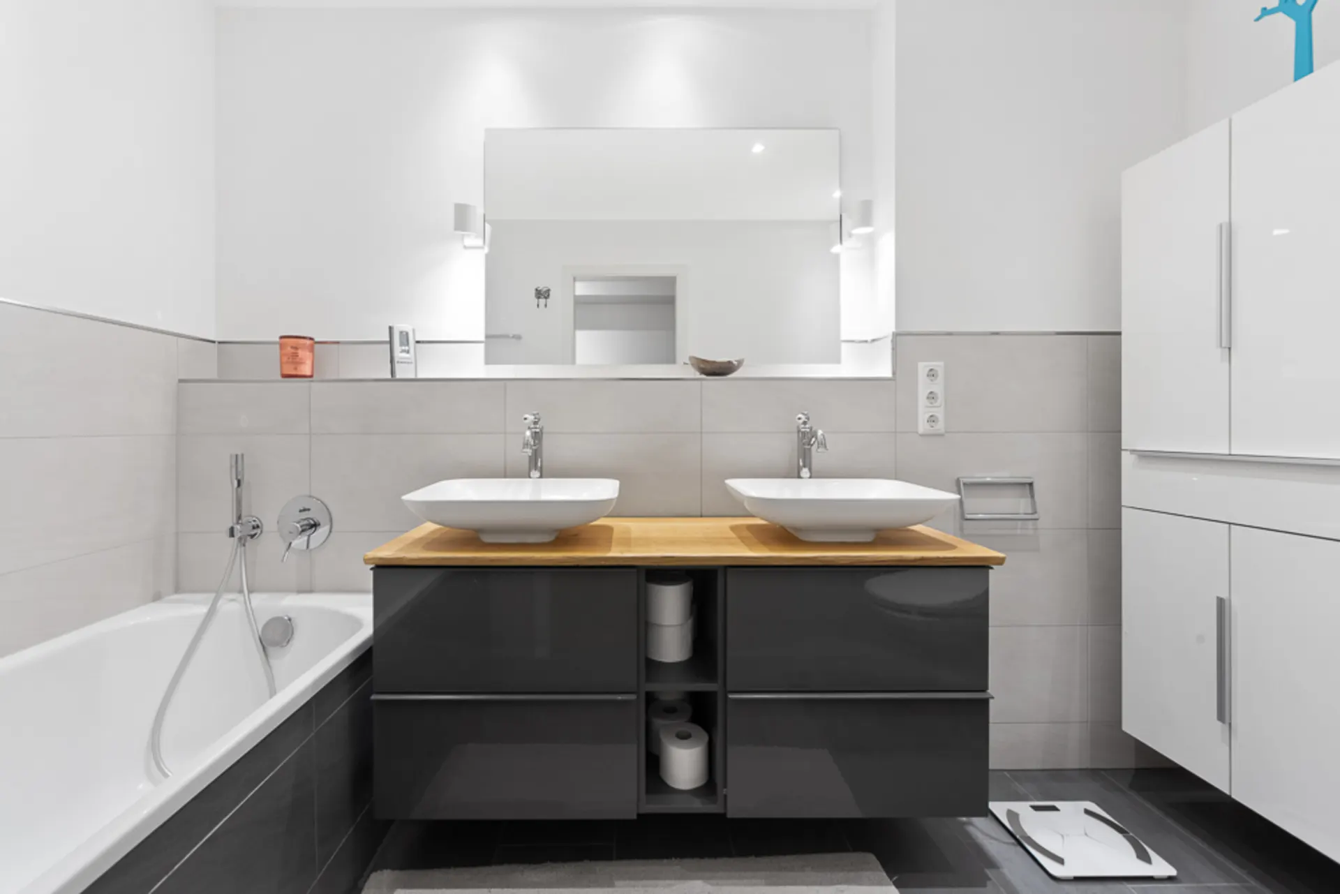 Modernes Badezimmer mit zwei Waschbecken, Spiegel, Badewanne und weißen Schränken.