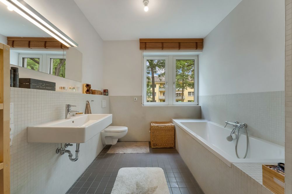 Modernes Badezimmer mit Badewanne, Waschbecken, Toilette und Fenster mit Blick nach draußen.