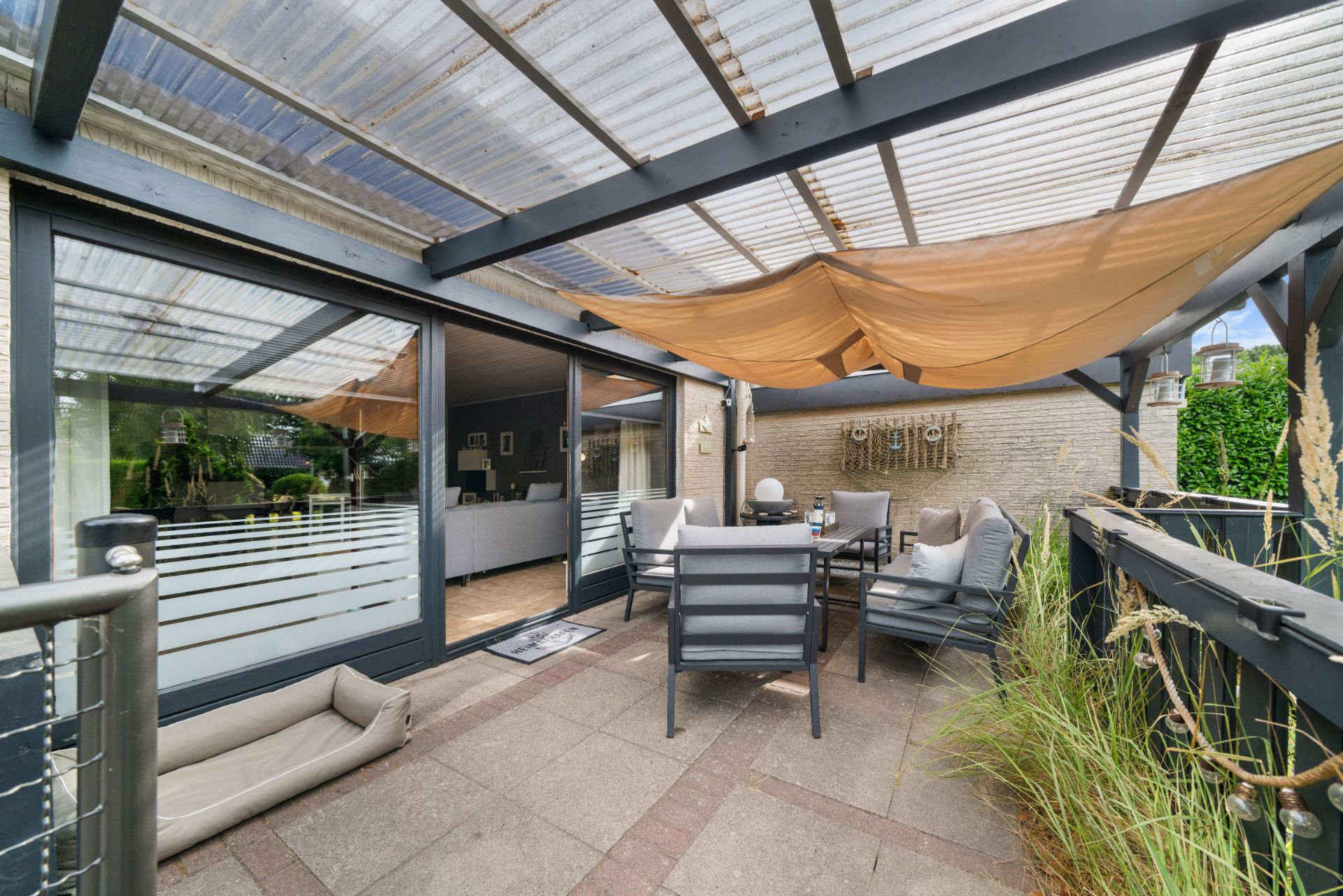 Überdachte Terrasse mit Sitzgruppe, Hundebett und Dekorationen an der Wand.