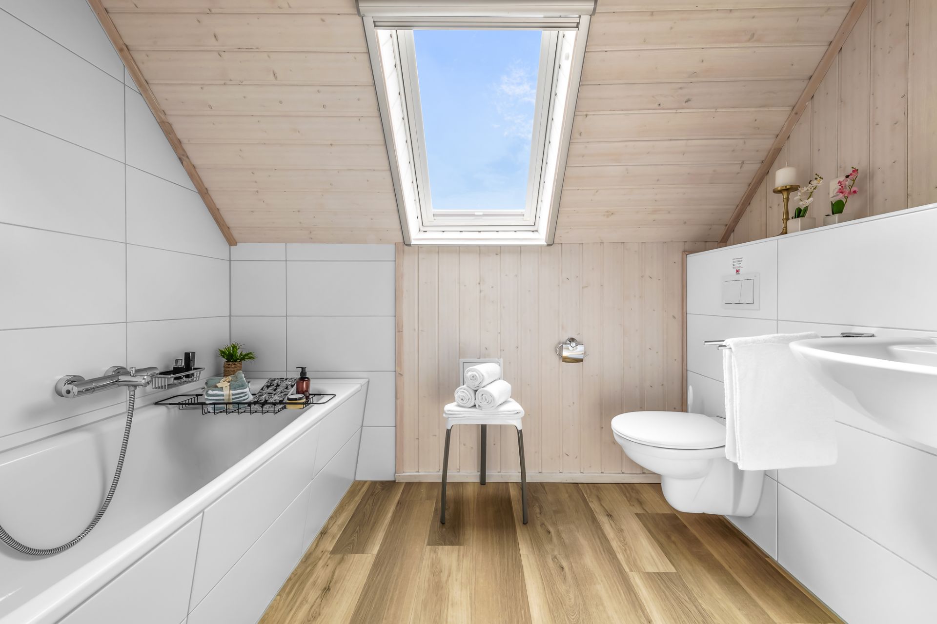 Helles Badezimmer mit Badewanne, WC, Waschbecken und Dachfenster unter einer Schräge.