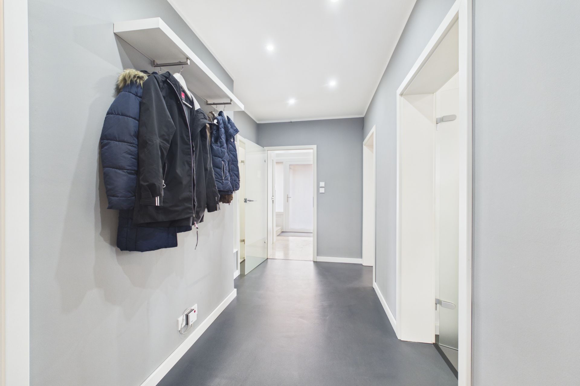 Heller Flur mit grauen Wänden, Kleiderhaken und mehreren Jacken an der Wand.