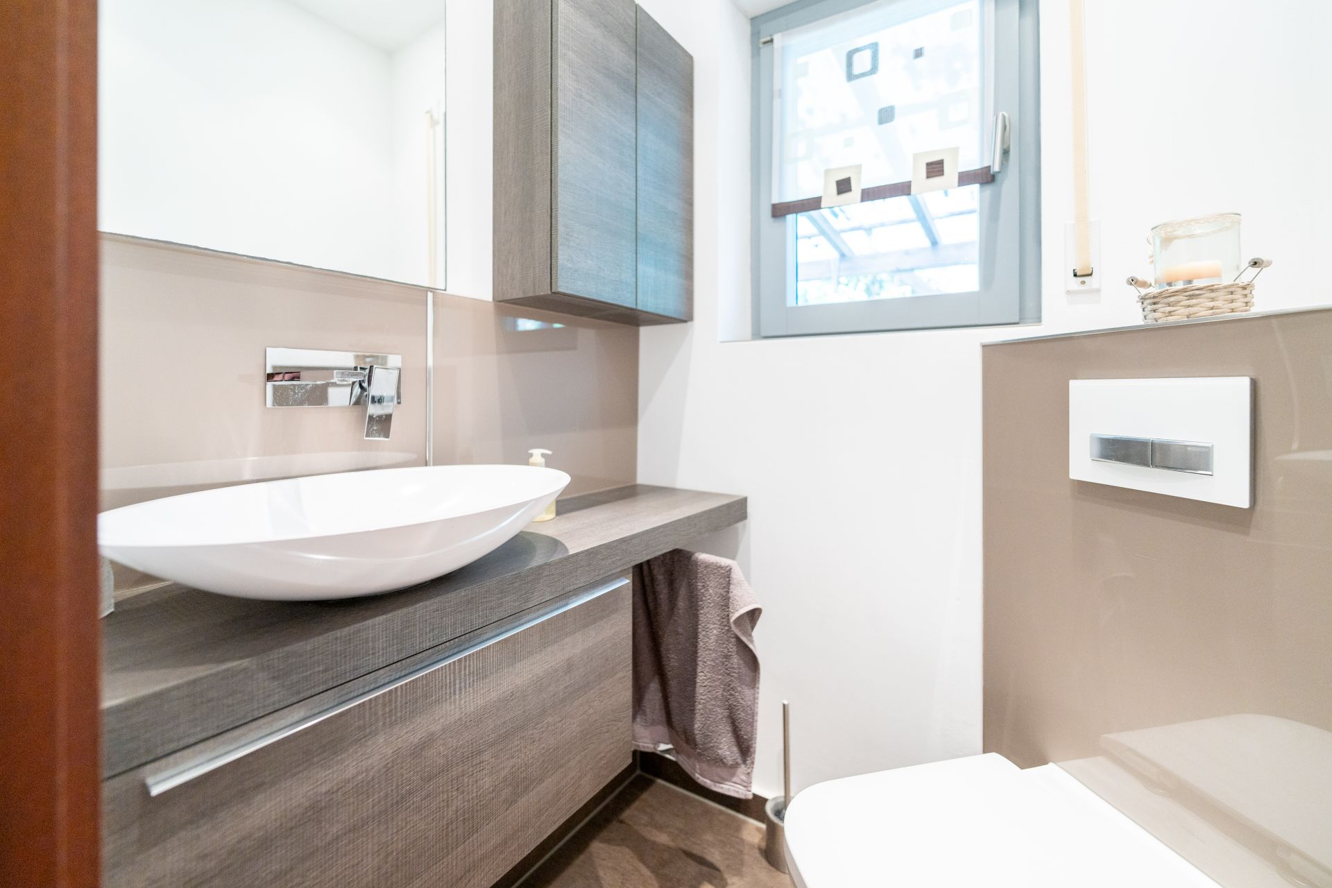 Modernes Badezimmer mit Waschbecken, Spiegel, Fenster und Toilettenspülung.