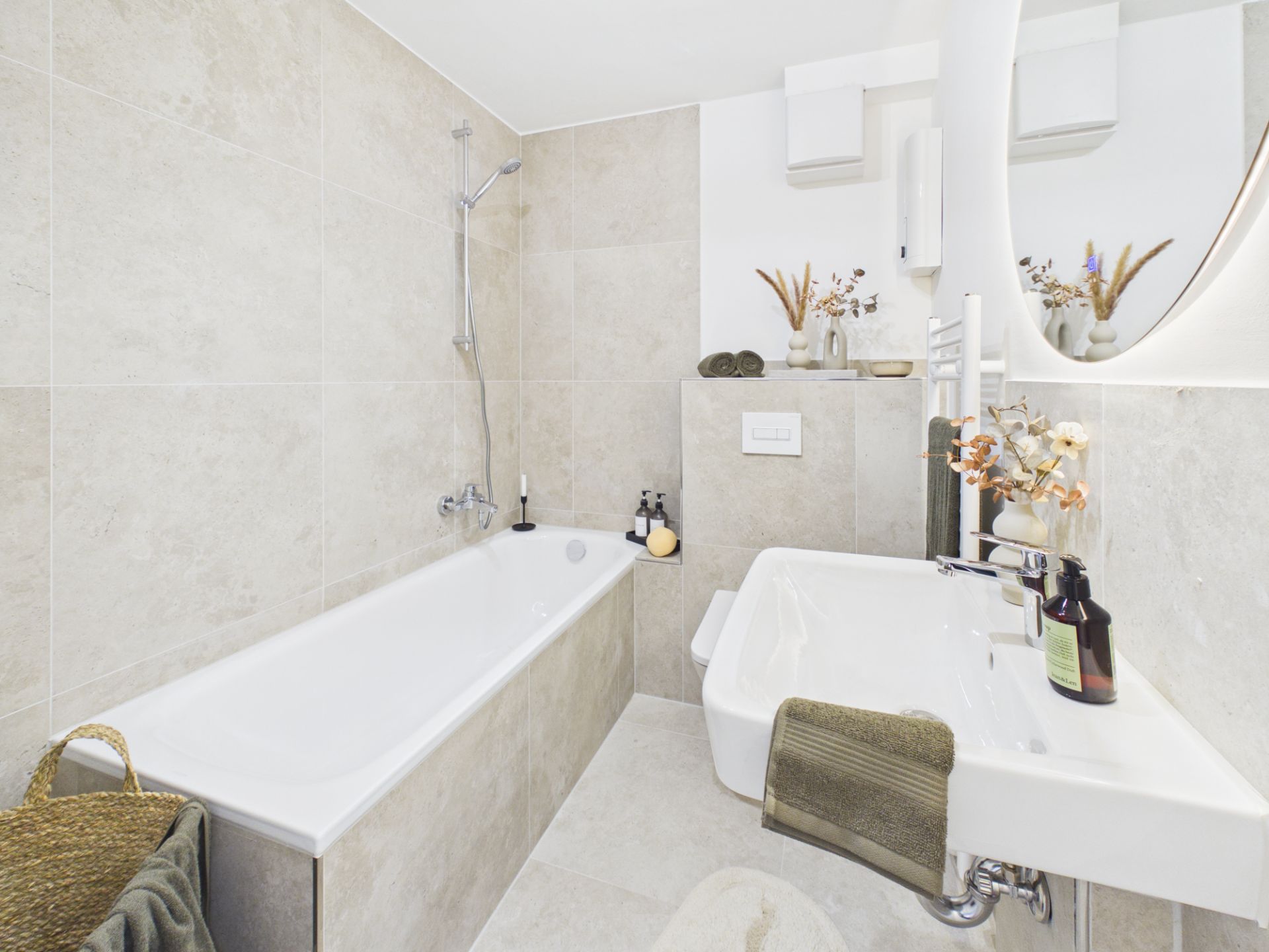 Modernes Bad mit Badewanne, Waschbecken, Spiegel und dekorativen Elementen auf beigen Fliesen.