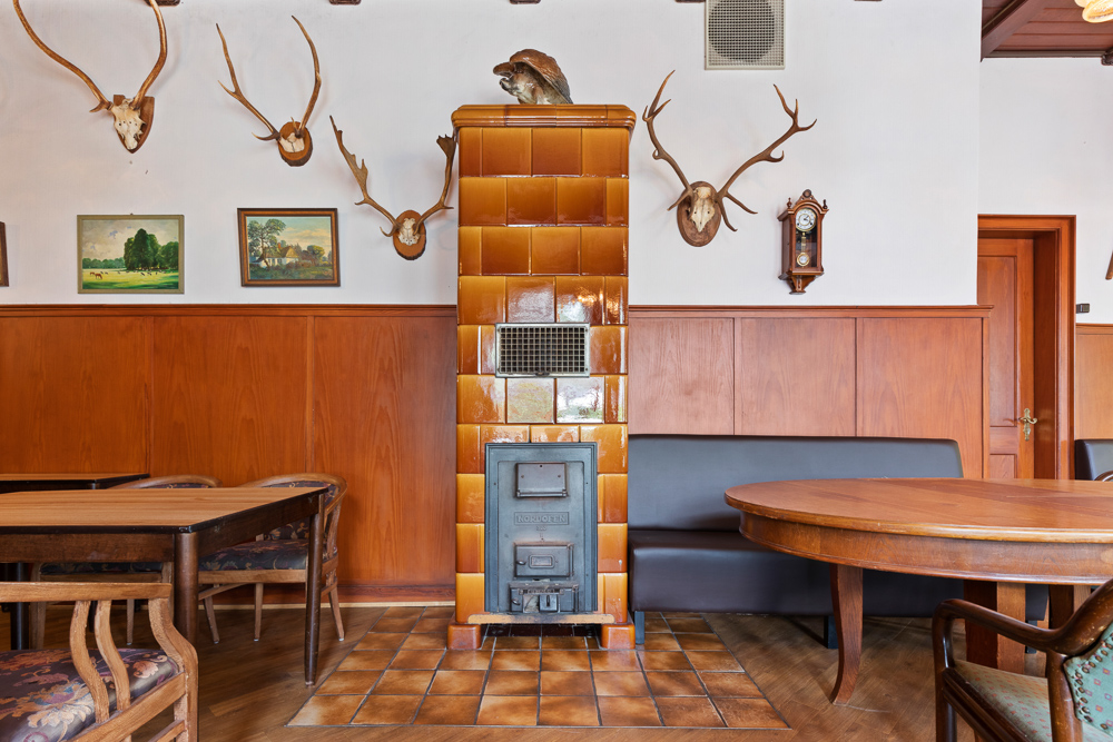Wohnzimmer mit Kachelofen, Holzmöbeln, Geweihen und Bildern an der Wand.
