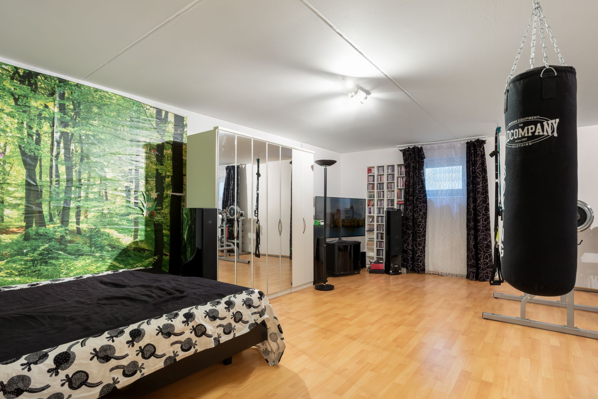 Geräumiges Schlafzimmer mit Boxsack, Spiegel-Schrank und großem Wandbild eines Waldes.