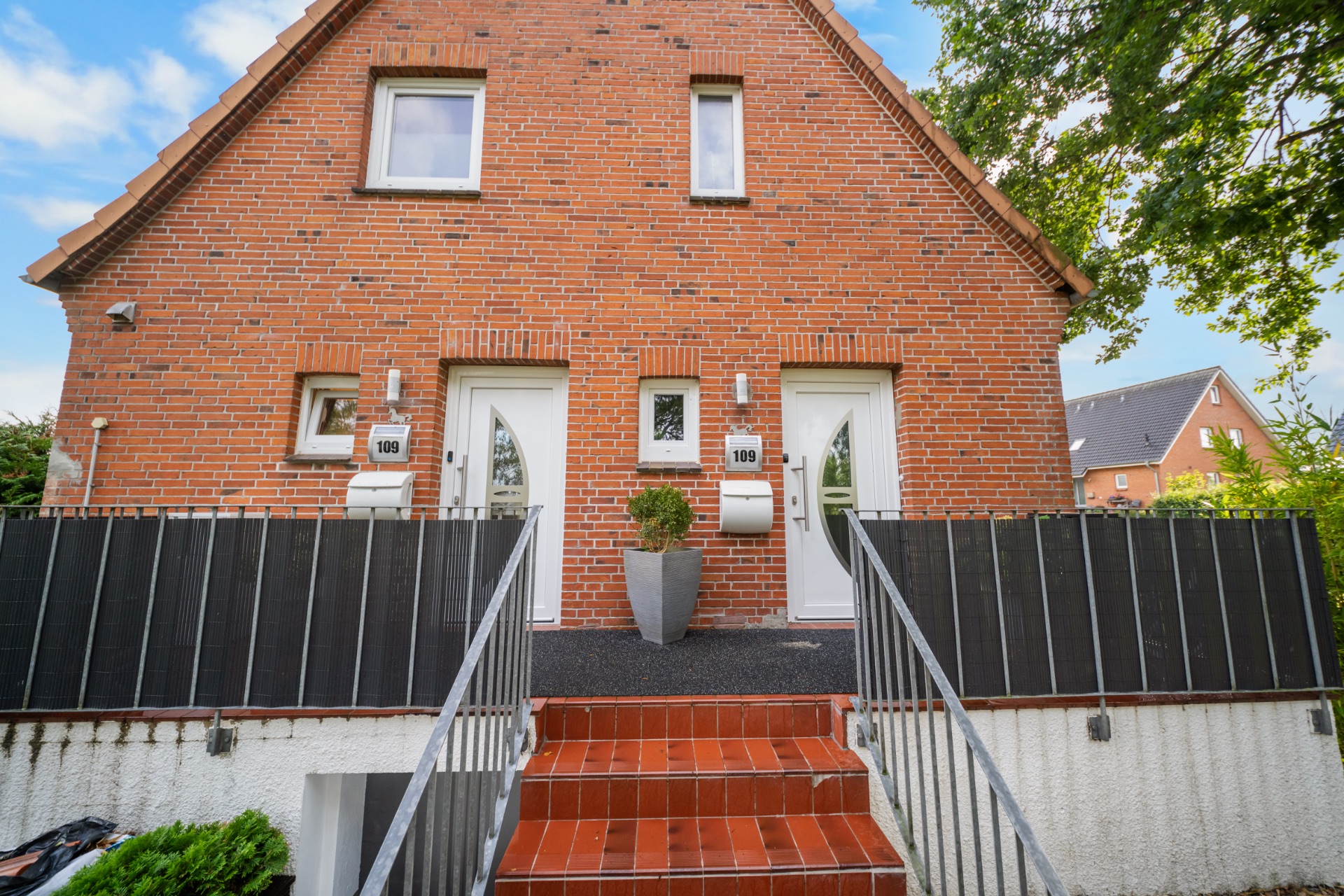 Eingang eines roten Backstein-Doppelhauses mit zwei weißen Türen und Treppe.