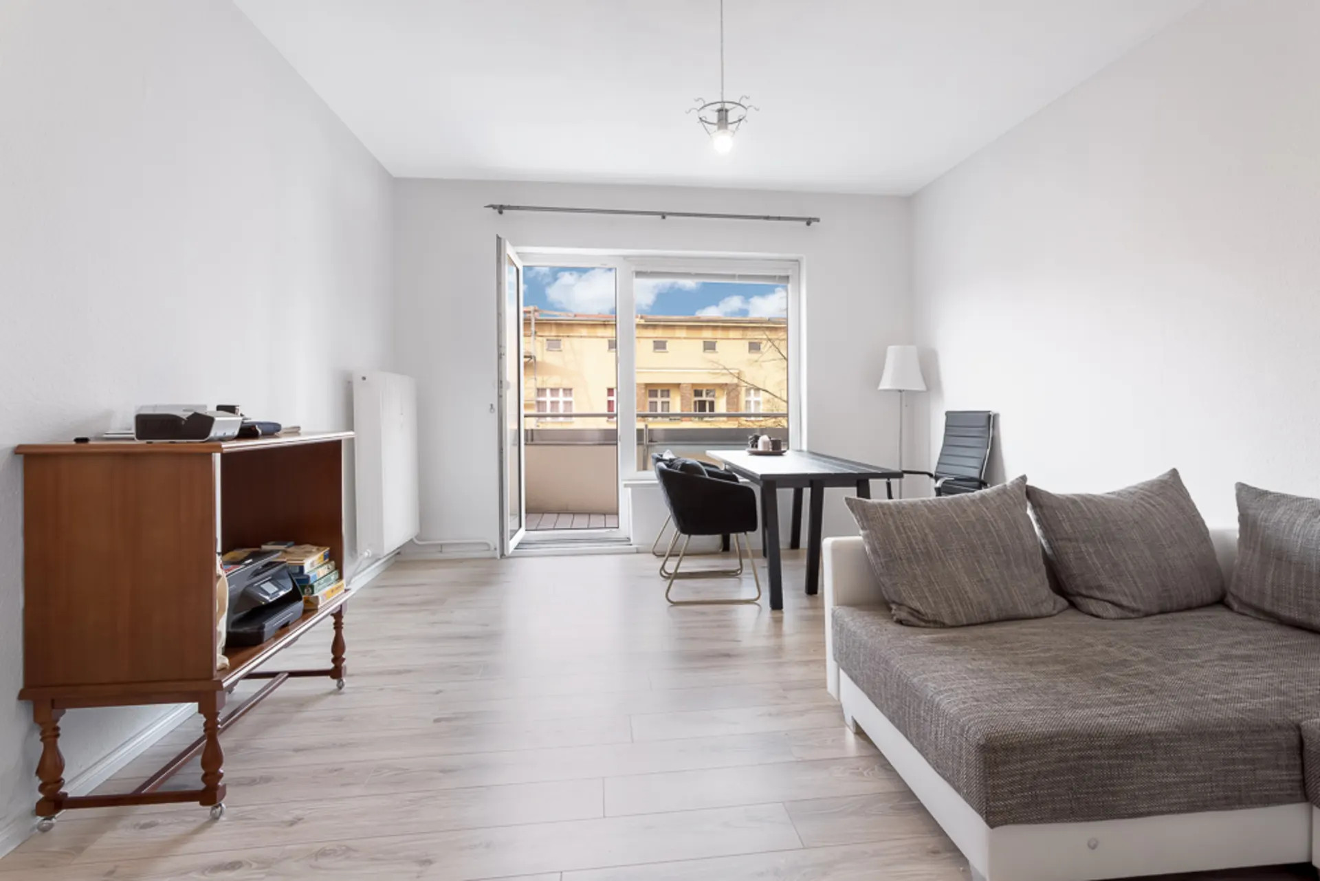 Helles Wohnzimmer mit Sofa, Esstisch, Stühlen, Regal und Zugang zu einem Balkon.