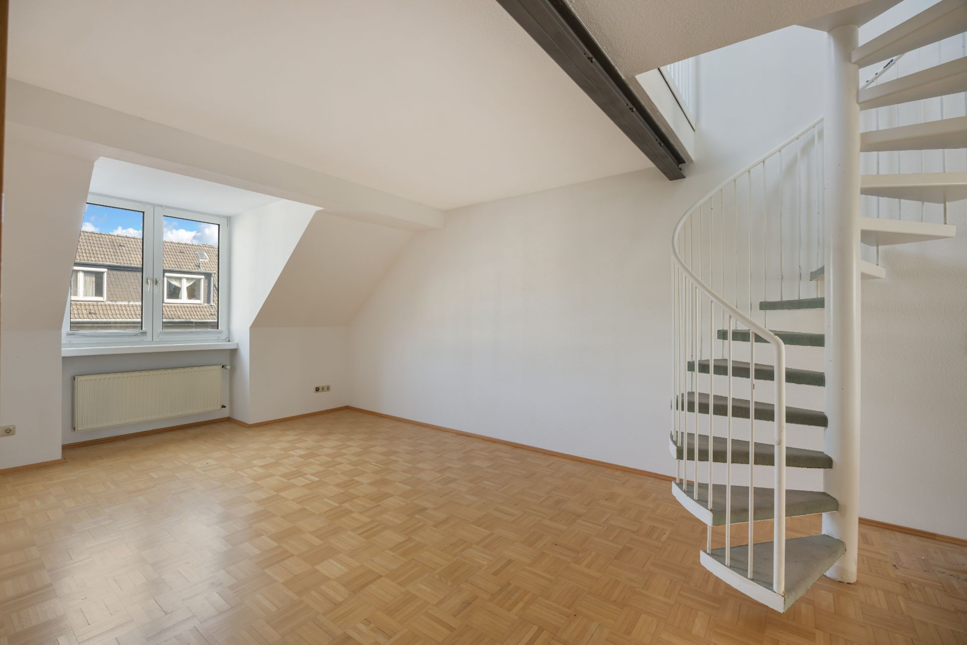 Helles Zimmer mit Parkettboden, großem Fenster und weißer Wendeltreppe.