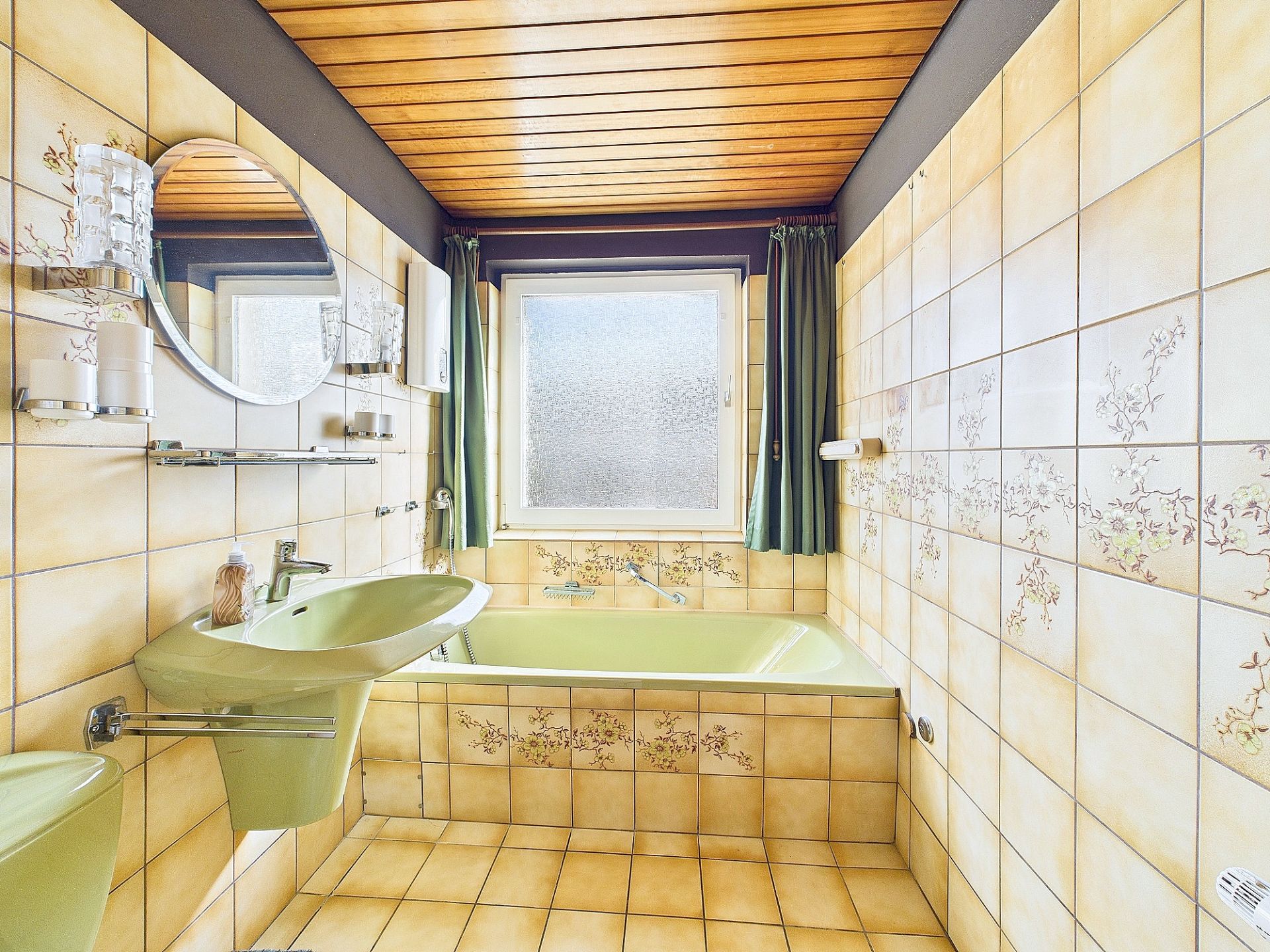 Badezimmer mit grüner Badewanne und Waschbecken, gelben Fliesen und einem Fenster mit Vorhängen.