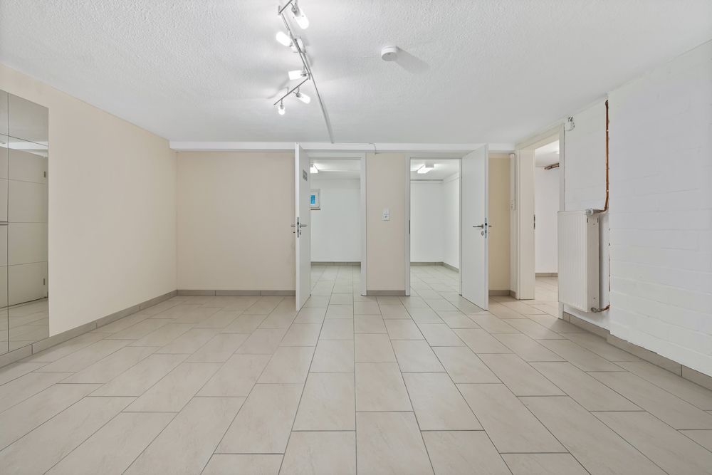 Heller Kellerraum mit Fliesenboden, drei offenen Türen und Heizkörper an der Wand.