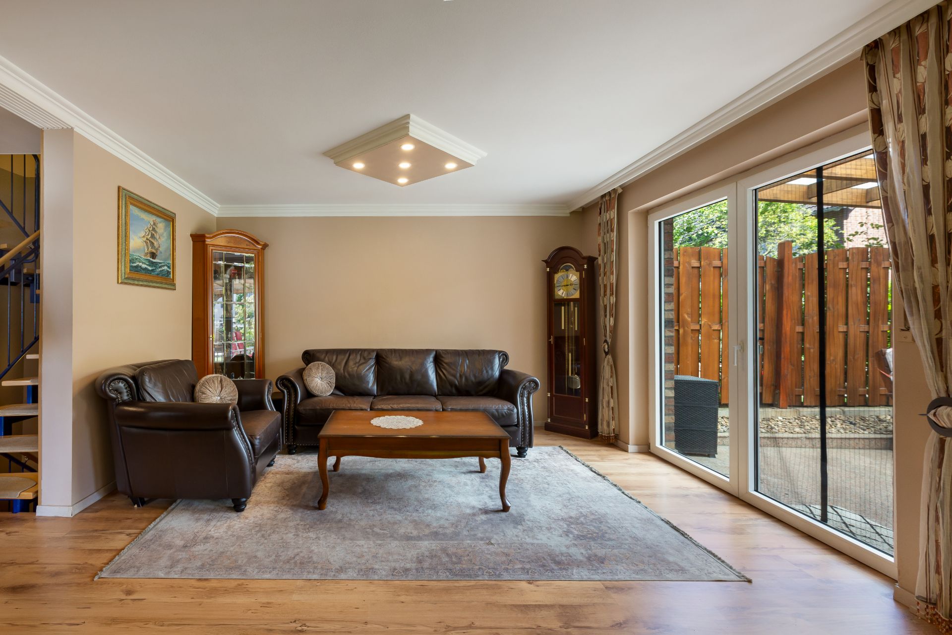 Wohnzimmer mit Ledersofa, Sessel, Couchtisch, Teppich und großem Fenster zur Terrasse.