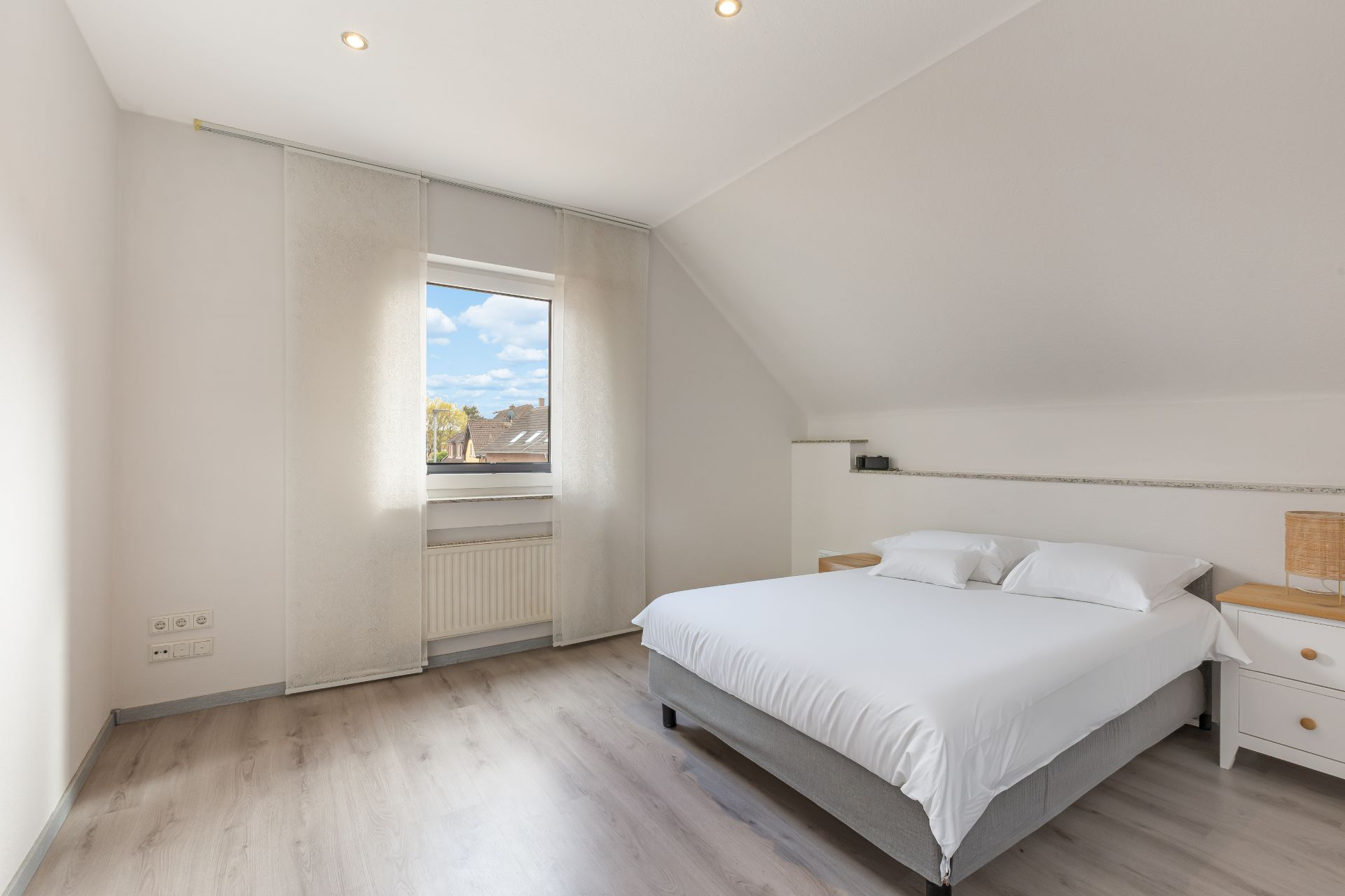 Helles Schlafzimmer mit großem Bett, zwei Nachttischen und Fenster mit Blick nach draußen.