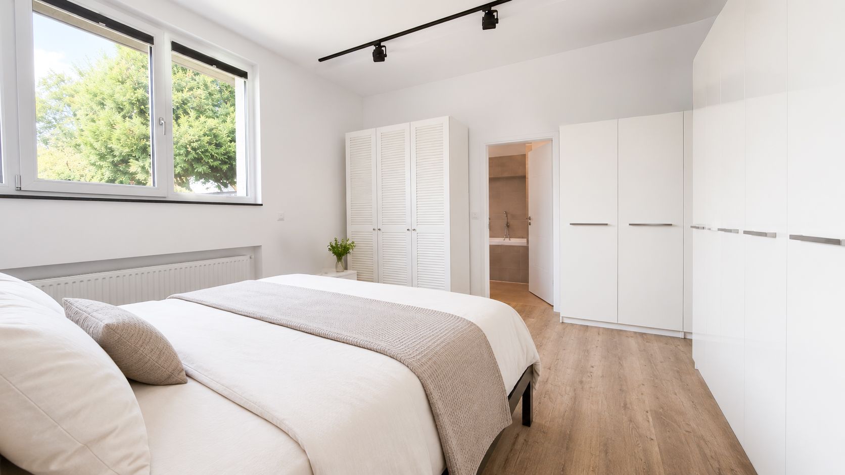 Helles Schlafzimmer mit Doppelbett, weißen Schränken und großem Fenster.