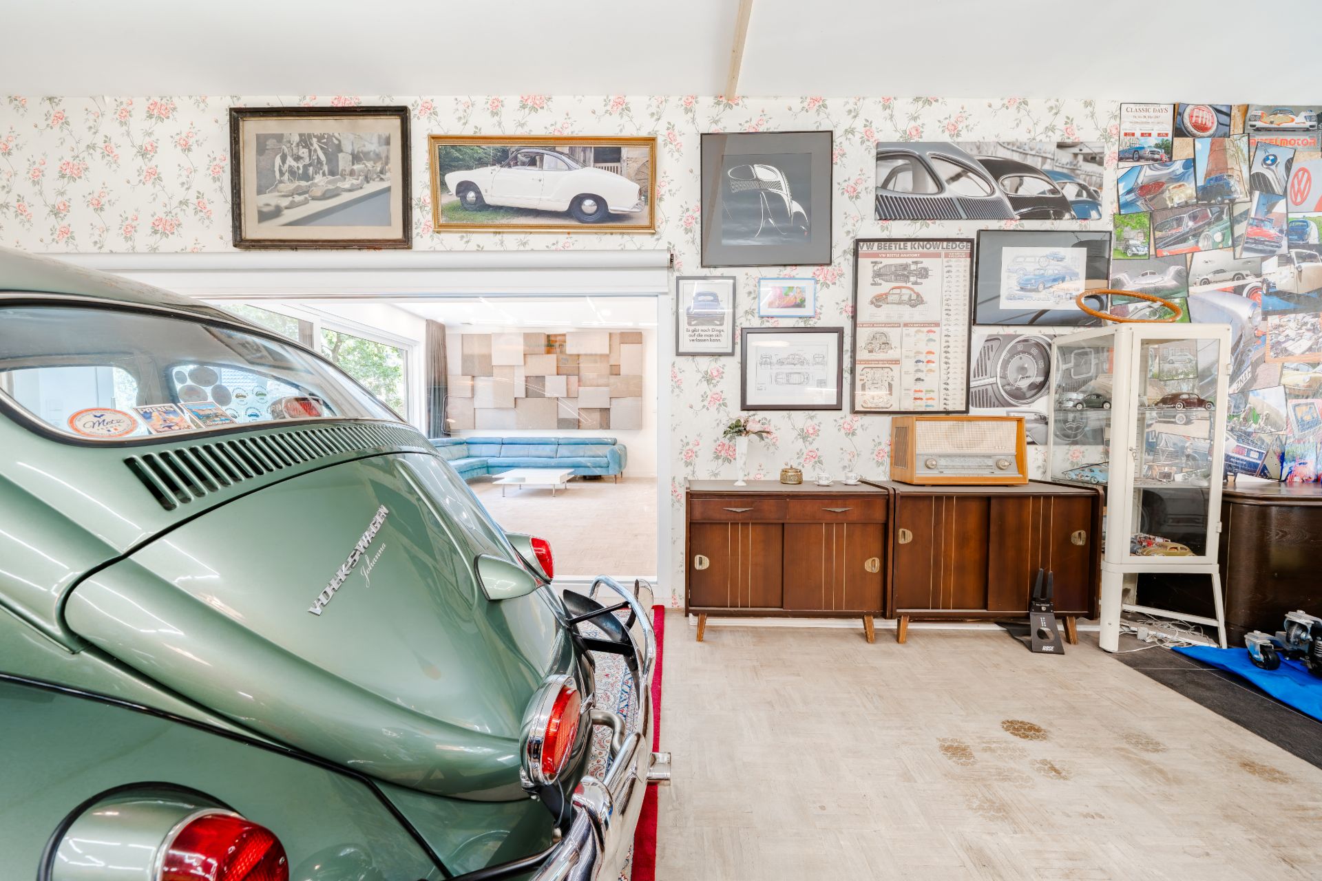 Grüne Oldtimer-Käfer in einer Garage mit Automobilpostern an der Wand und Holzmöbeln.