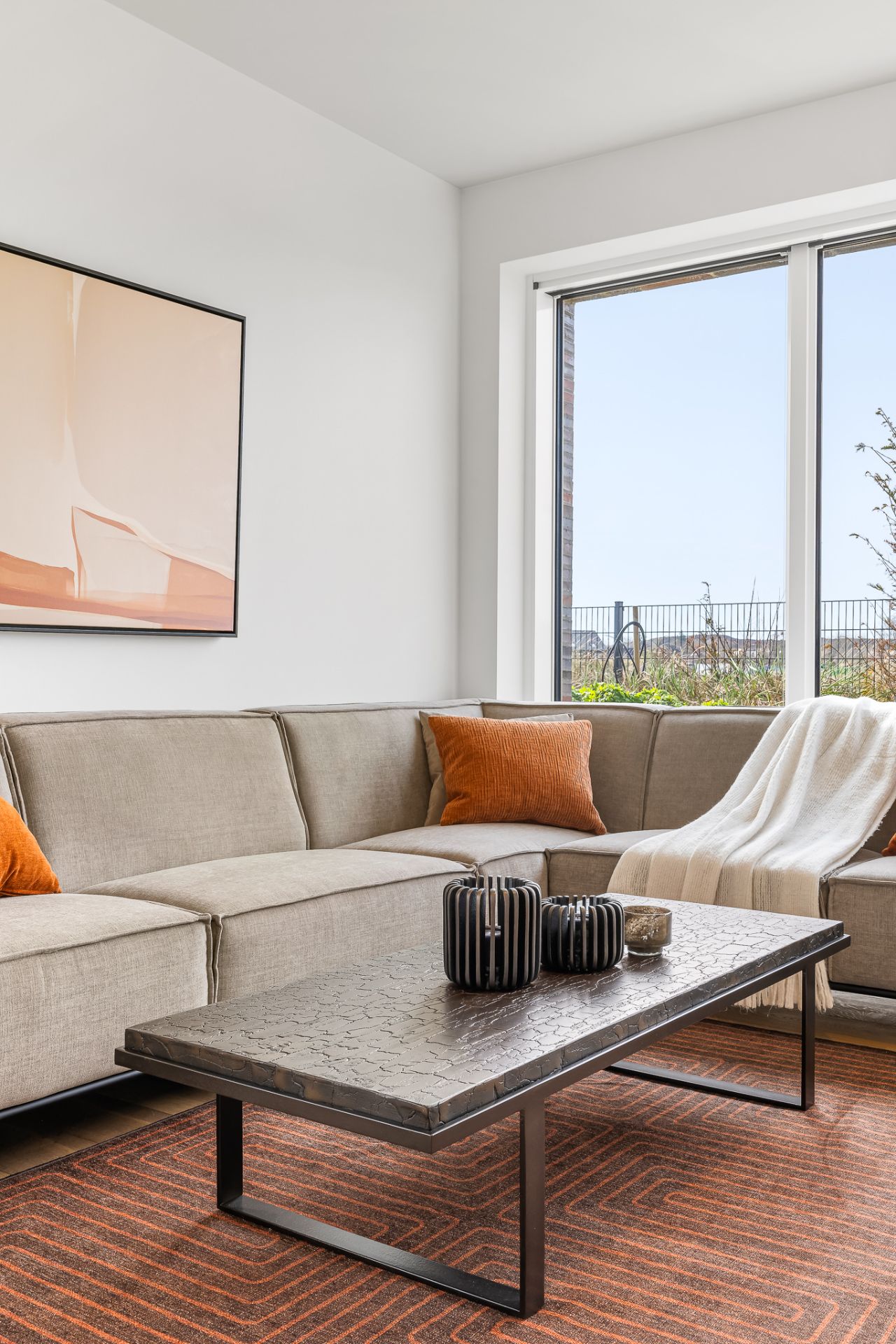 Helles Wohnzimmer mit Ecksofa, Couchtisch, orangen Kissen und großem Fenster.
