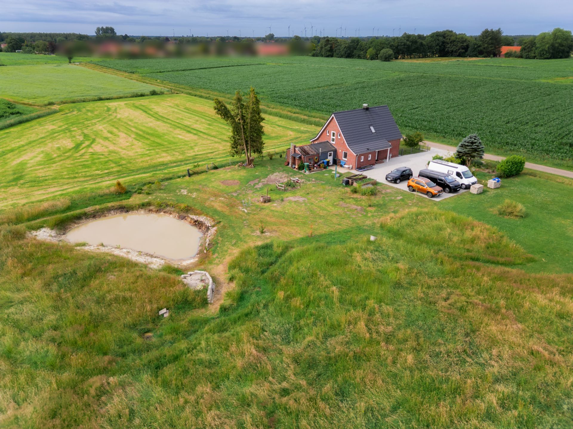 Backsteinhaus mit mehreren Autos, großem Garten und Teich, umgeben von Feldern.