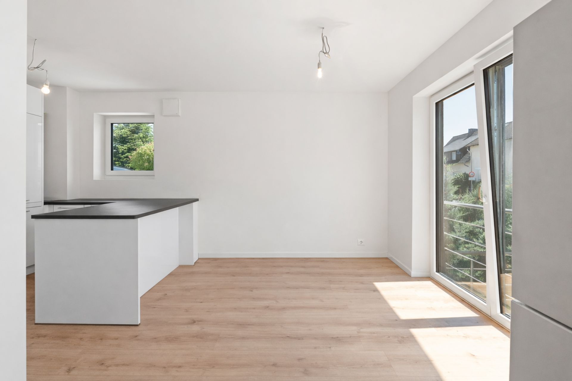 Helles Wohnzimmer mit offener Küche, Holzfußboden und großem Fenster mit Blick ins Grüne.