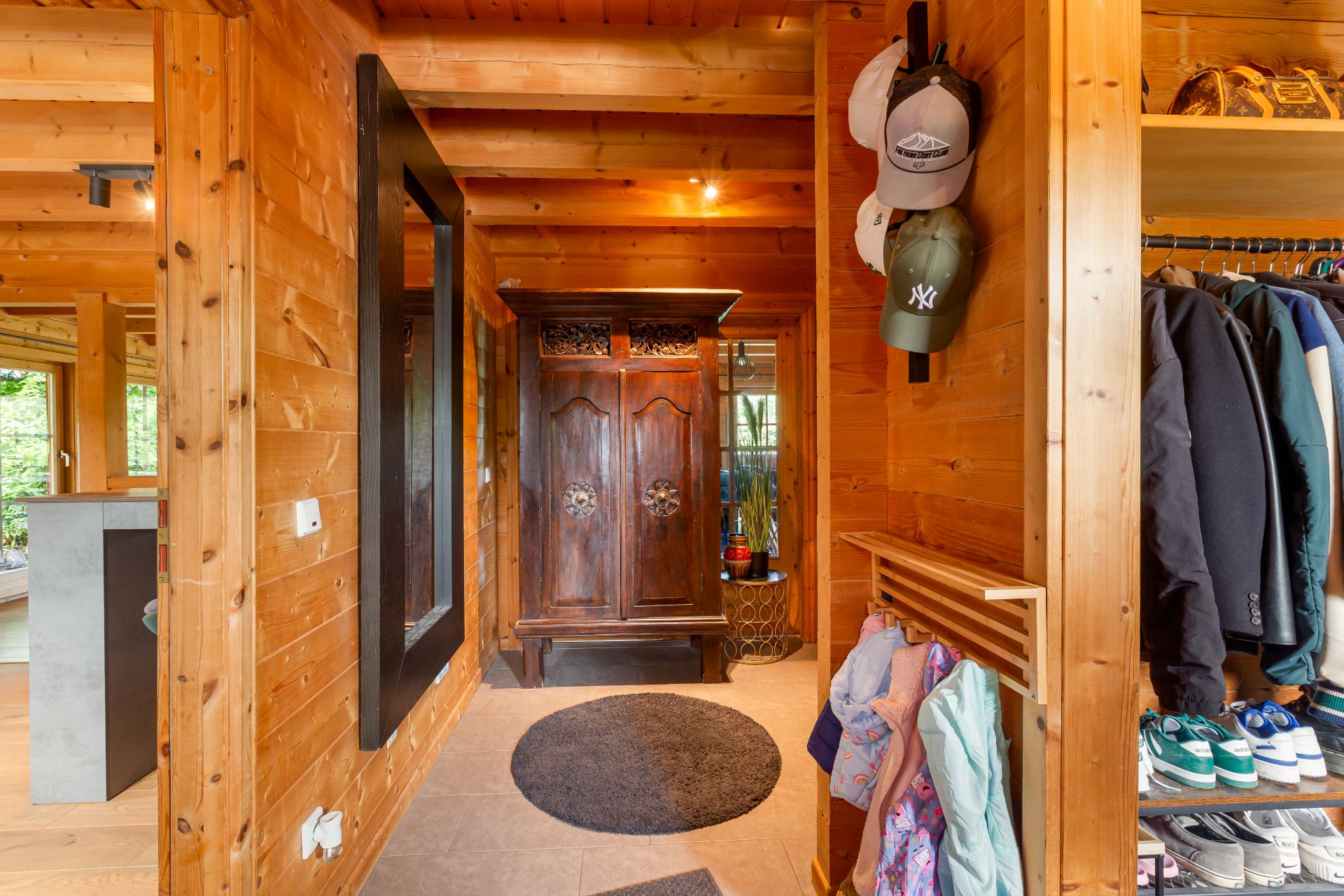 Holzflur mit Spiegel, Garderobe, Schuhregal und großem Schrank im Hintergrund.