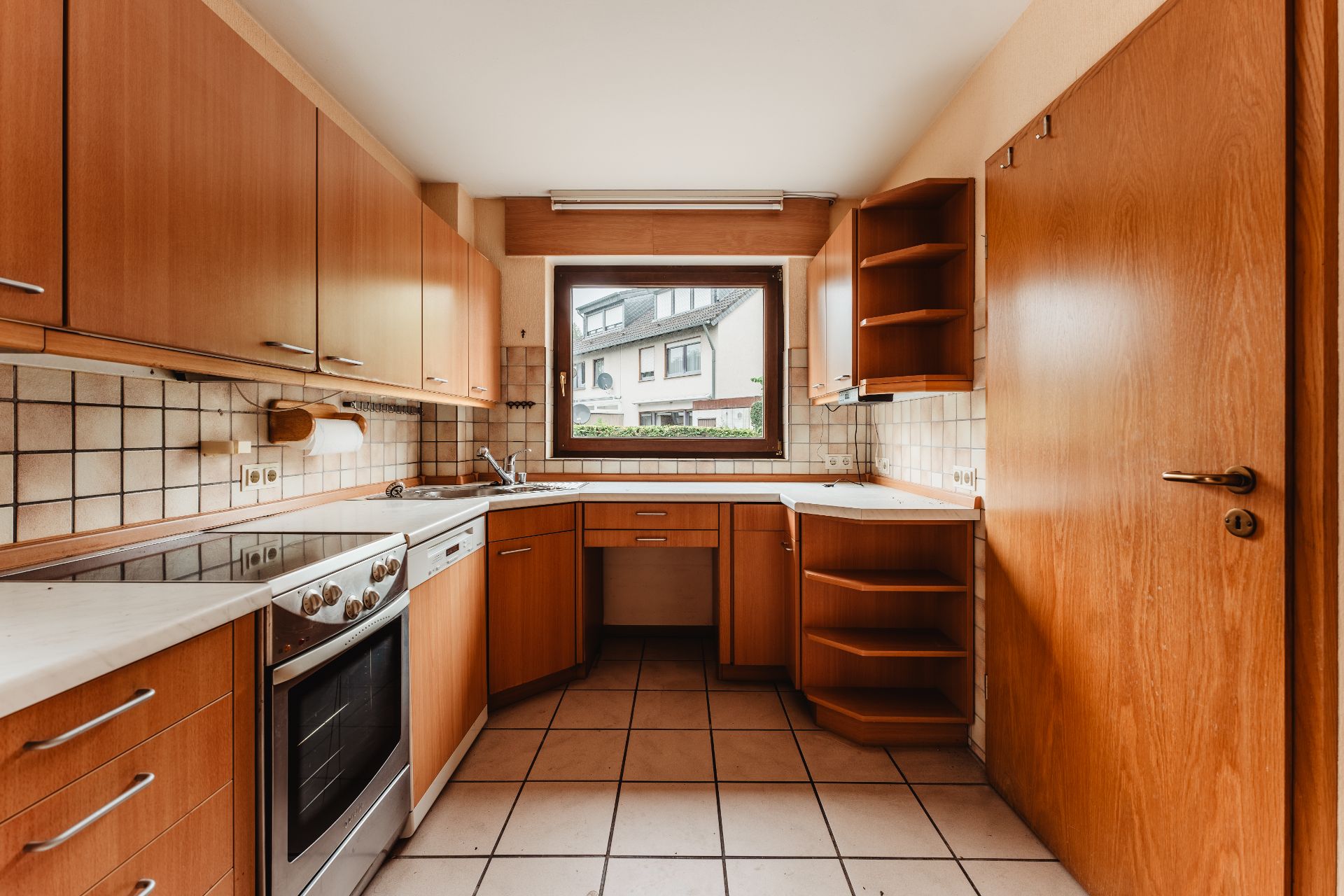 Küche mit Holzschränken, Elektroherd, Spüle und Fenster mit Blick nach draußen.