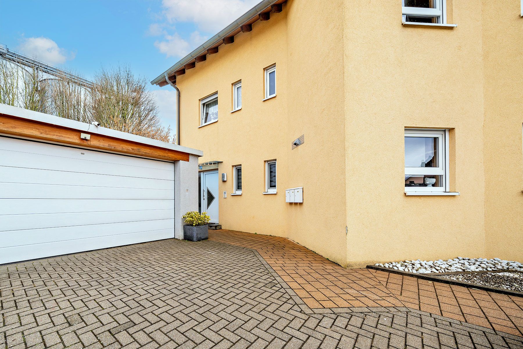 Eingang eines Wohnhauses mit gelber Fassade, Garage und gepflastertem Hof.