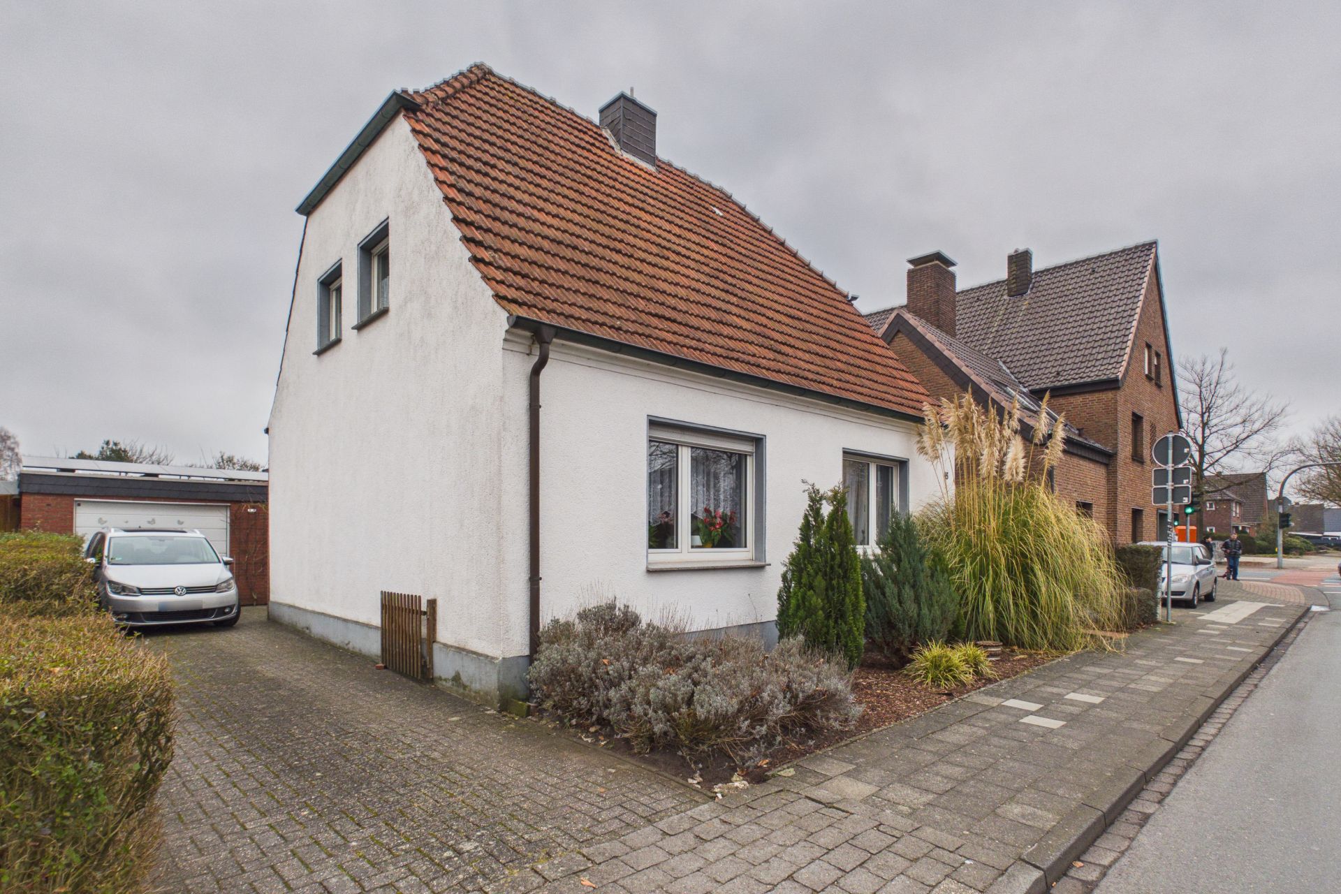 Weißes Einfamilienhaus mit rotem Satteldach, Einfahrt und Vorgarten neben der Straße.