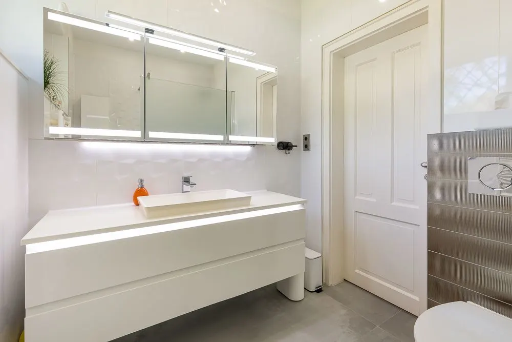 Modernes Badezimmer mit weißem Waschtisch, Spiegel und geschlossener Tür.