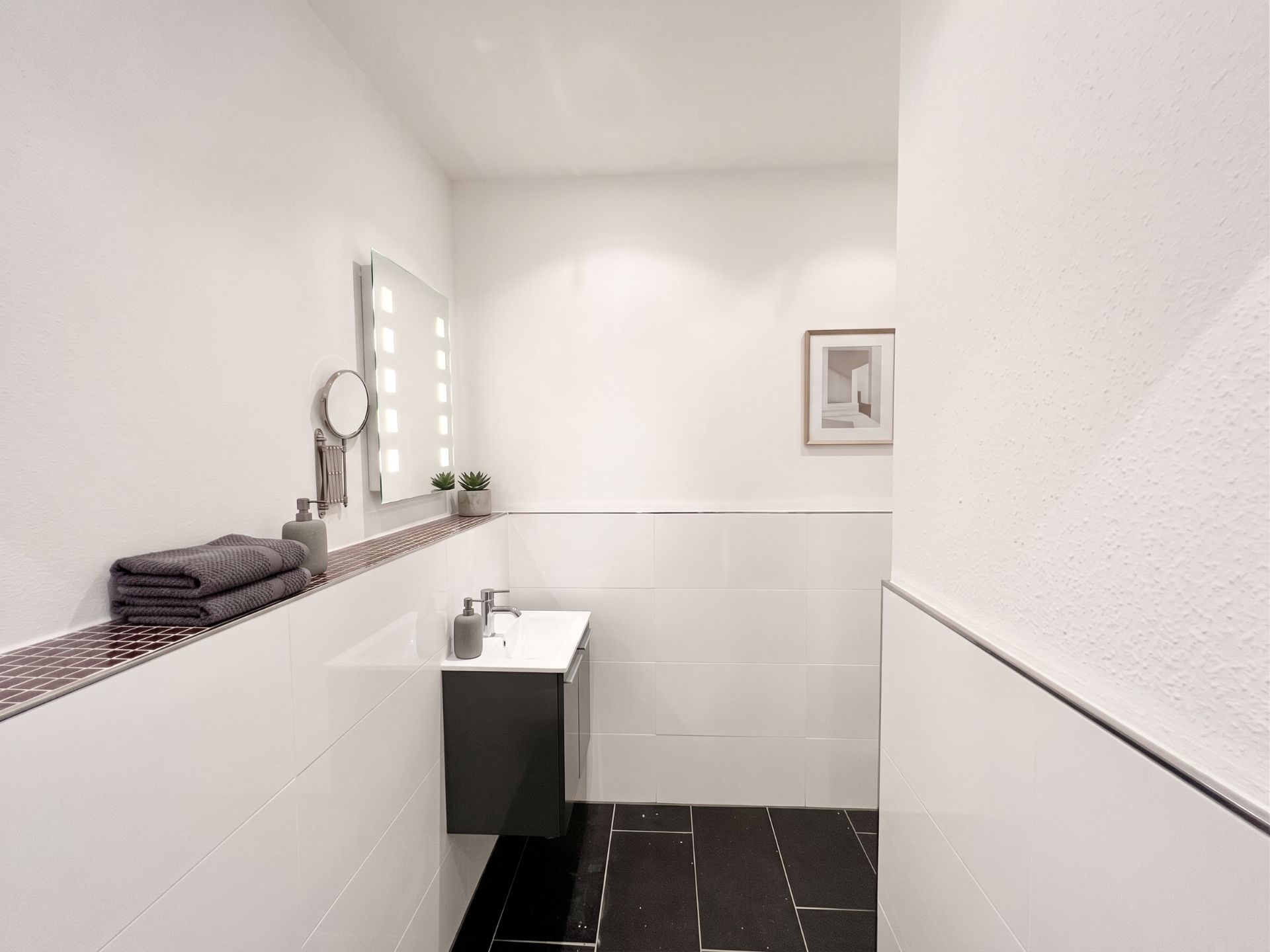 Modernes Badezimmer mit kleinem Waschbecken, Spiegel, Handtüchern und Wandbild.