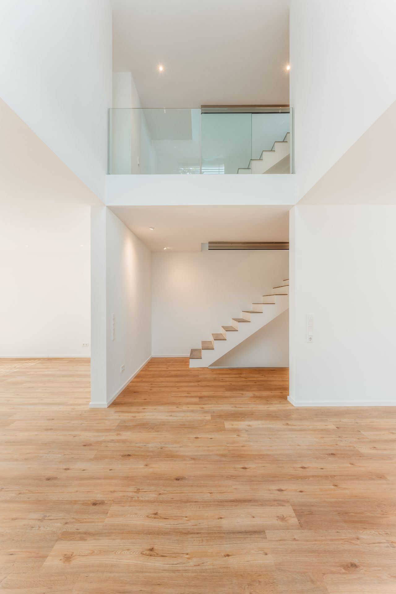 Heller Raum mit Holzfußboden und moderner Treppe mit Glasgeländer.