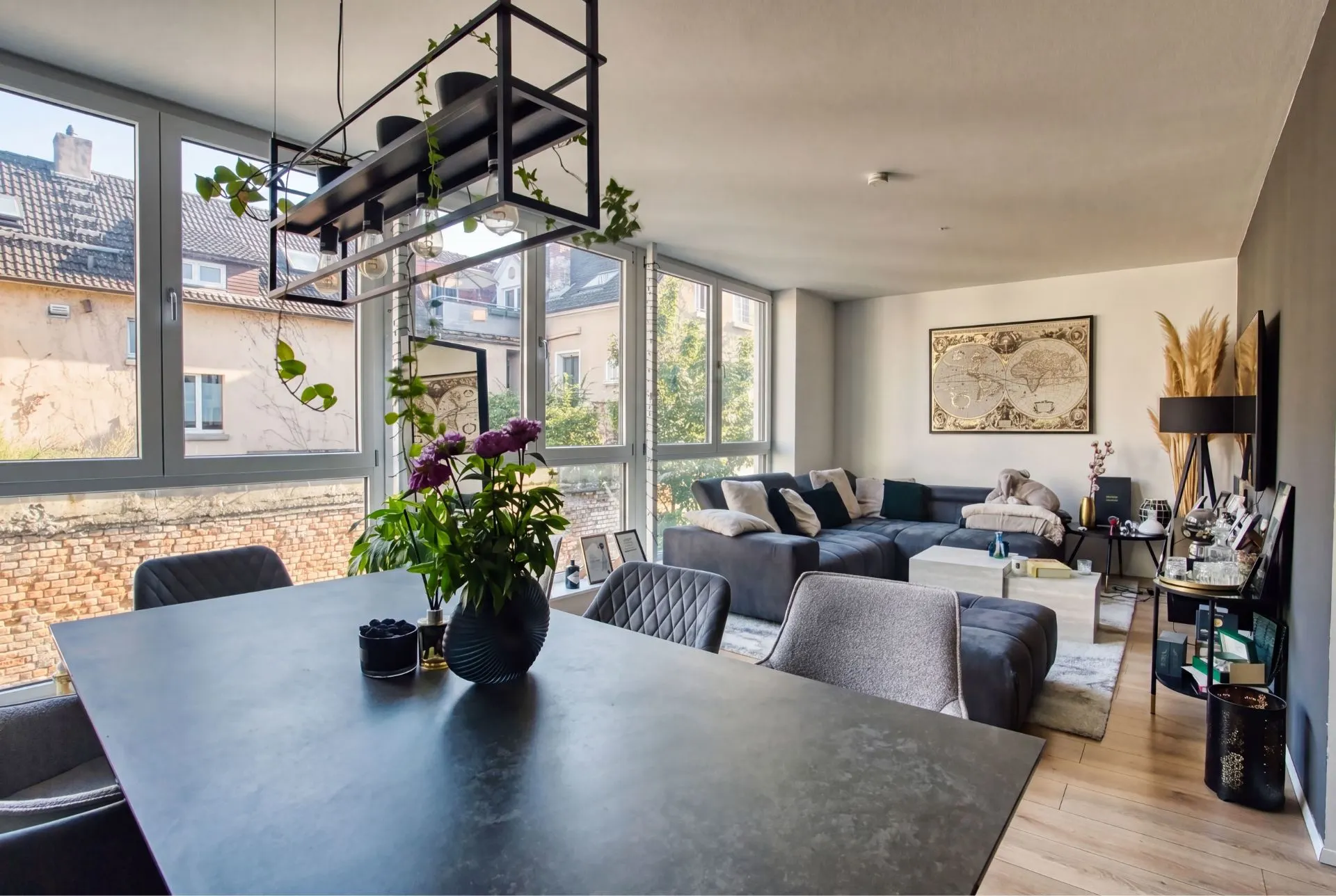 Modernes Wohnzimmer mit großem Sofa, Esstisch, vielen Fenstern und Zimmerpflanzen.