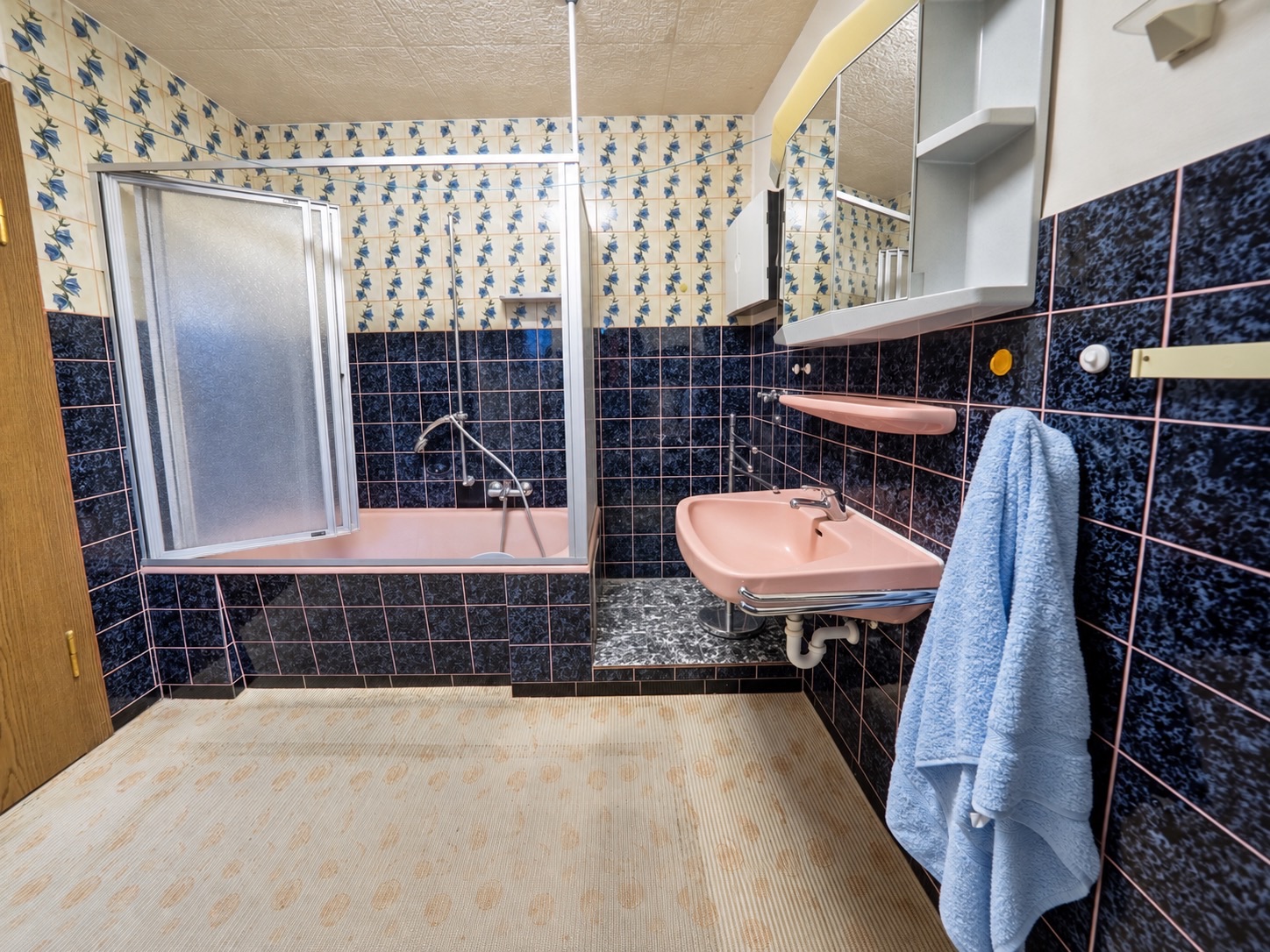 Badezimmer mit rosa Badewanne, rosa Waschbecken, Spiegel und blau gemusterten Fliesen.