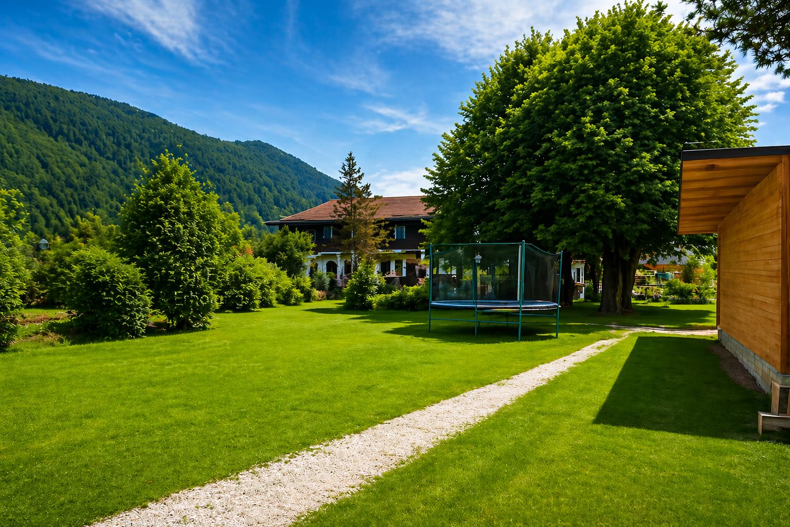 Großer grüner Garten mit Trampolin, Bäumen, Weg und Wohnhaus im Hintergrund.