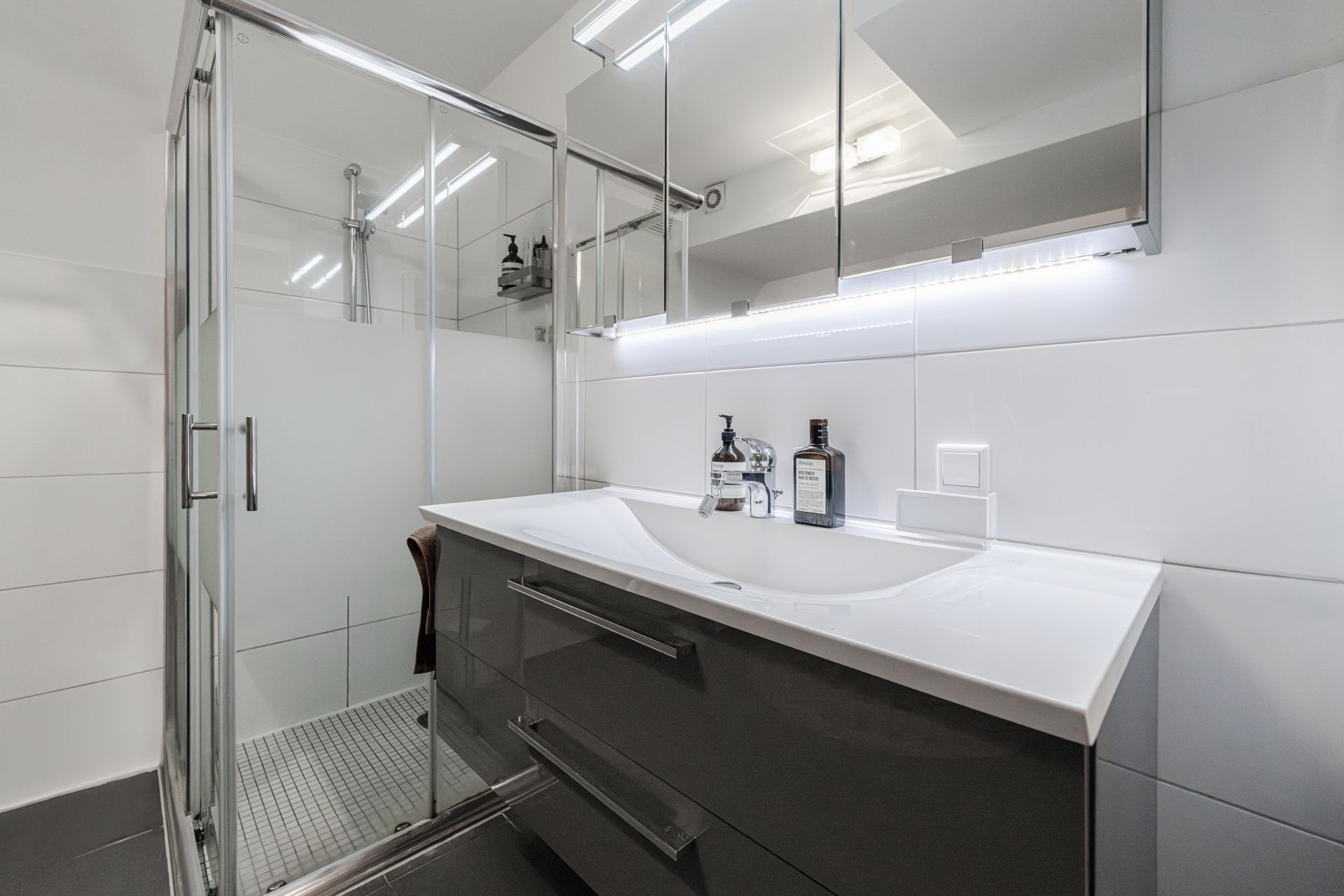 Modernes Badezimmer mit Glasdusche, Waschbecken, Spiegel und weißen Fliesen.