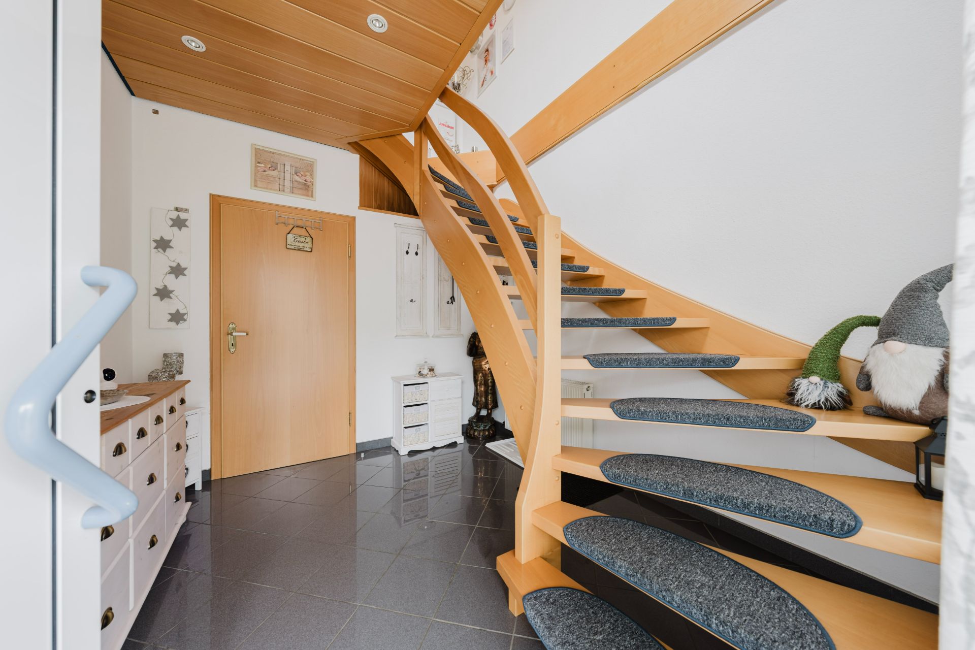 Heller Flur mit Holztreppe, Fliesenboden und Kommode, Eingangstür und Dekorationen sichtbar.