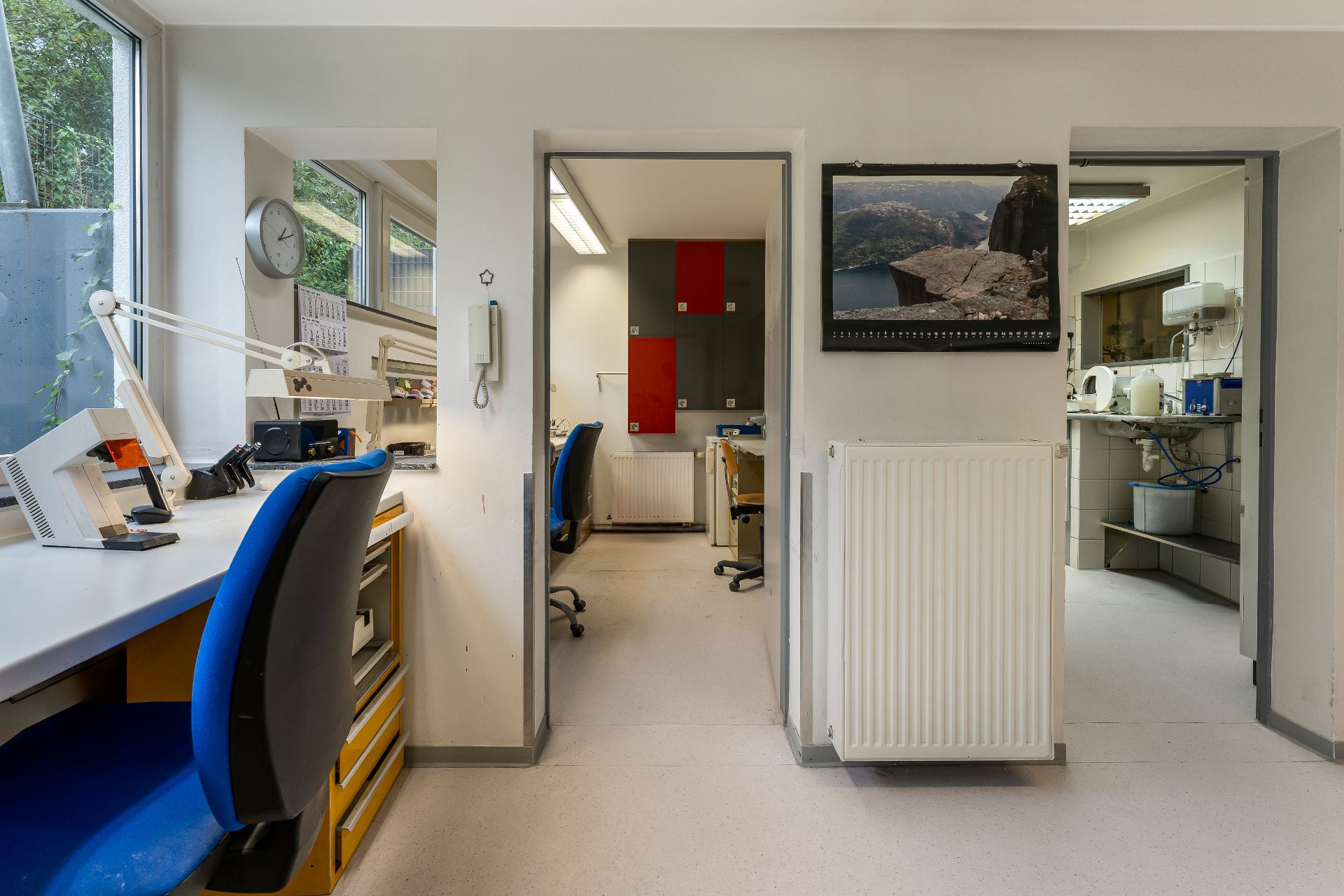 Heller Arbeitsraum mit Schreibtischen, blauen Stühlen und Blick in zwei weitere Räume.