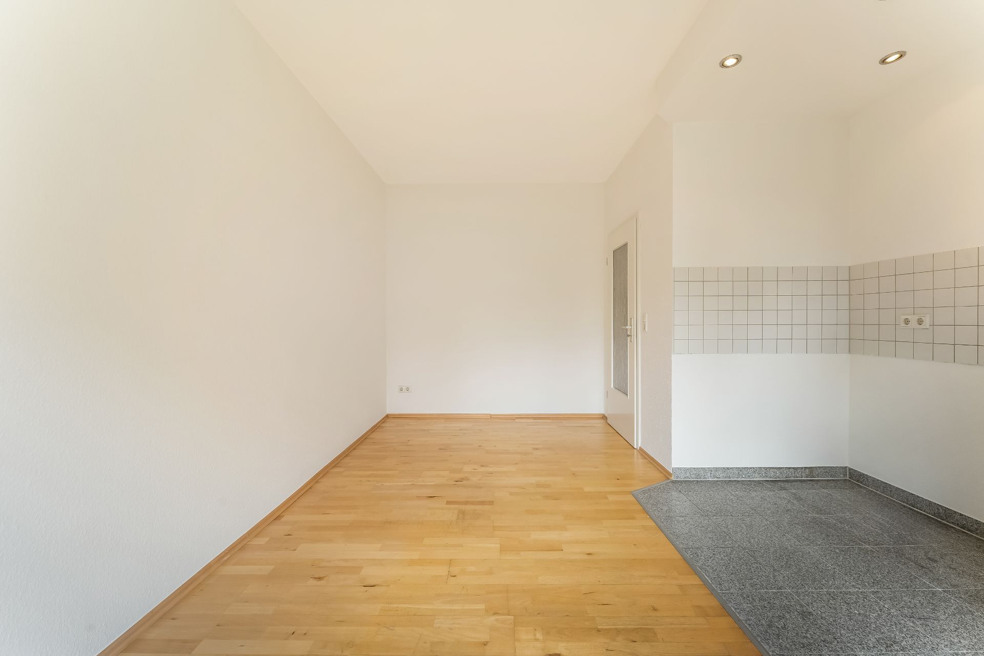 Leerer Raum mit hellem Holzboden und Fliesenbereich an der Wand mit weißen Fliesen.