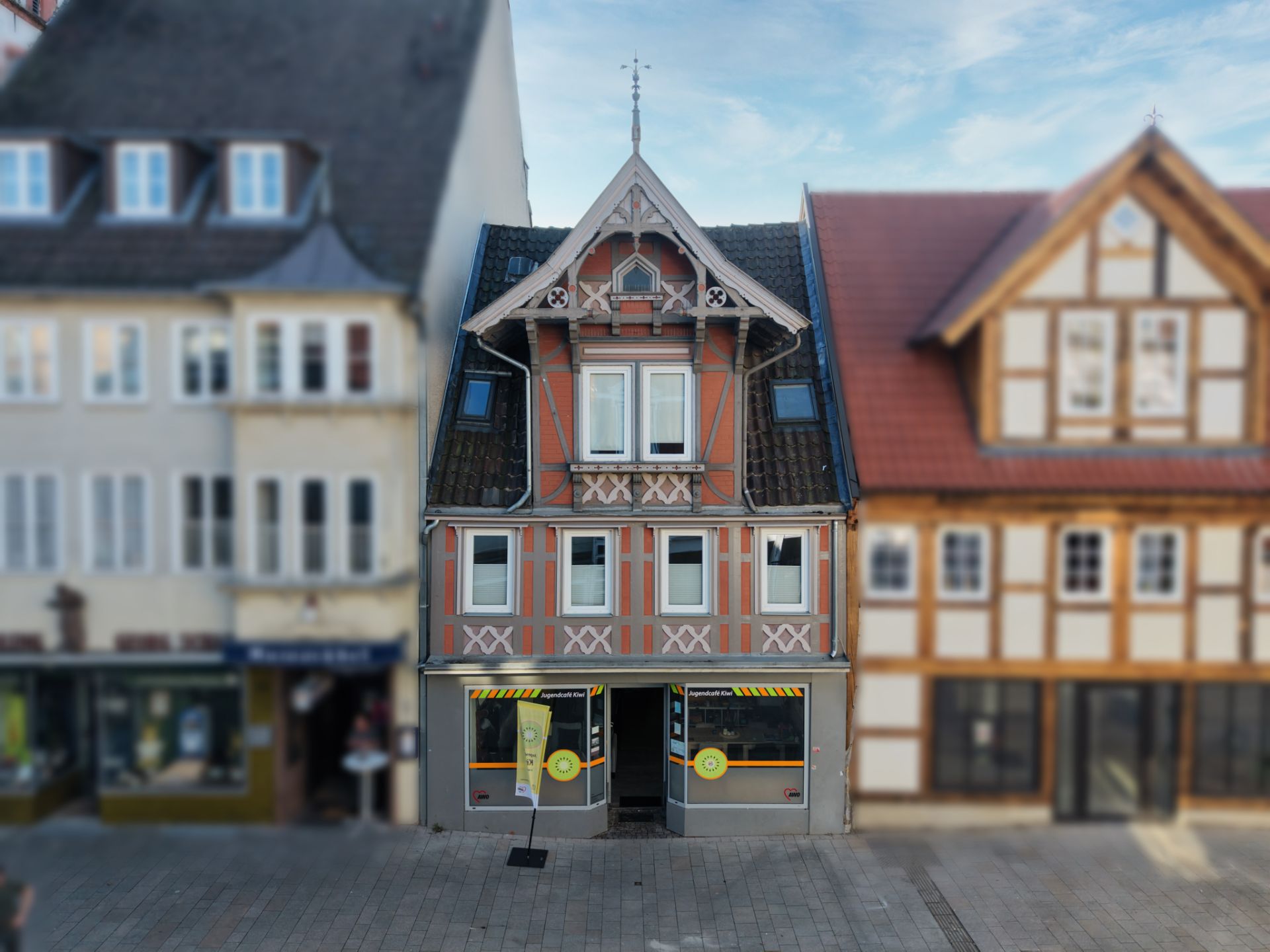 Fachwerkhaus mit zwei Etagen und Schaufenstern im Erdgeschoss, daneben weitere Häuser.