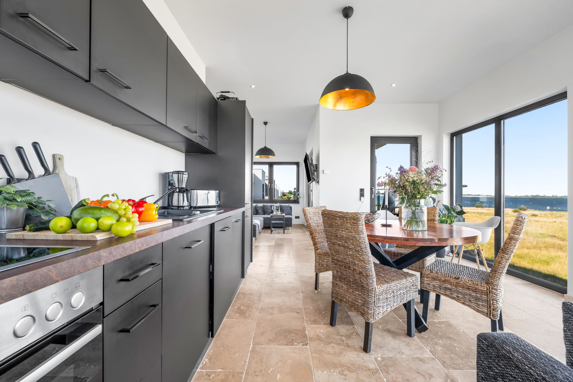 Moderne Küche mit schwarzen Schränken, Esstisch und großen Fenstern mit Blick ins Grüne.