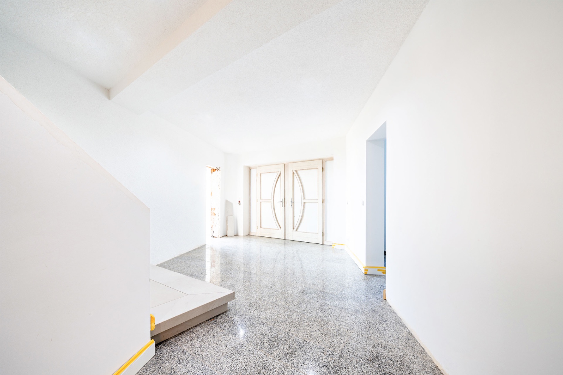 Heller Eingangsbereich mit großen Doppeltüren und glänzendem Boden, links eine Treppe.