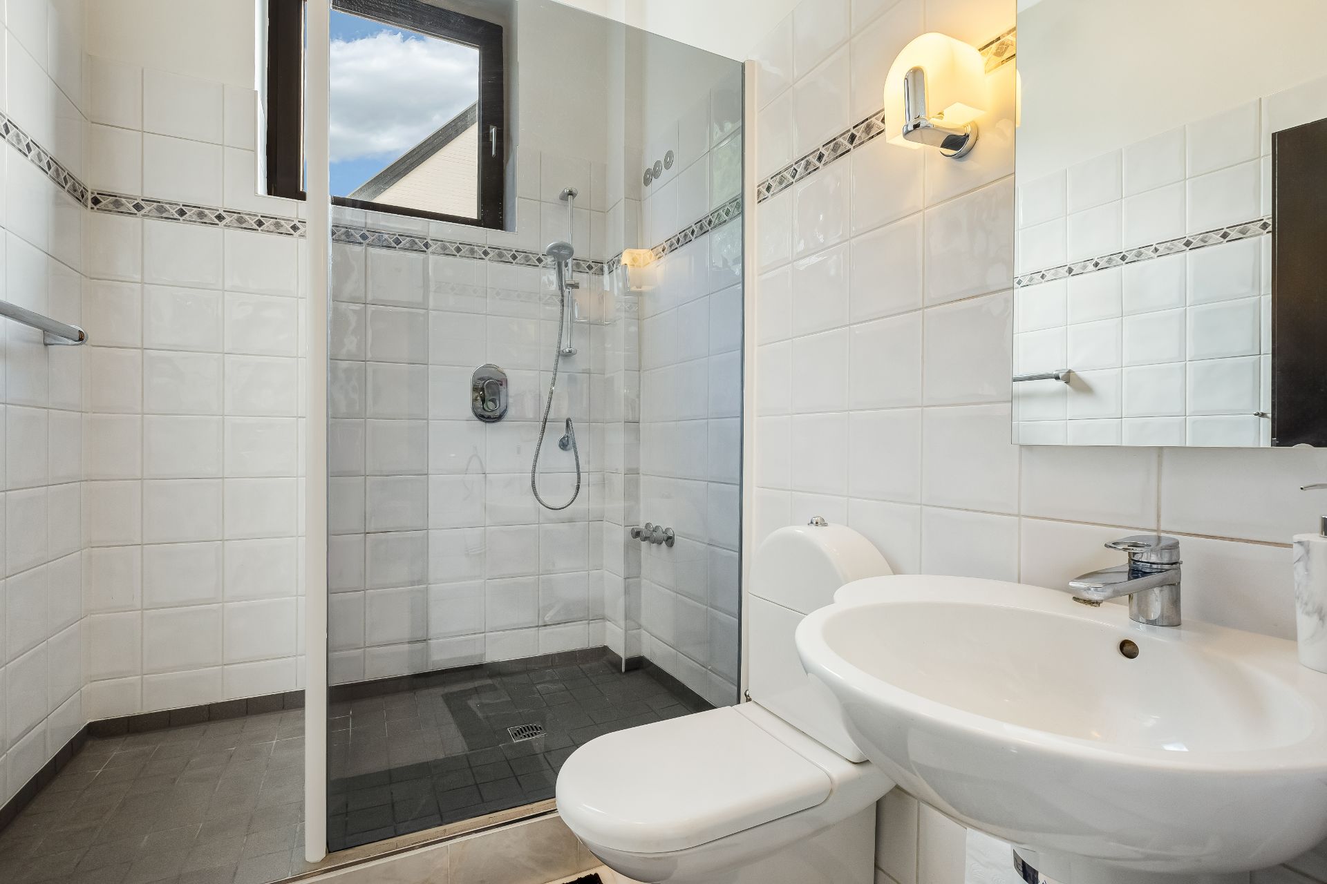 Helles Badezimmer mit Dusche, WC und Waschbecken, weiße Fliesen an den Wänden.