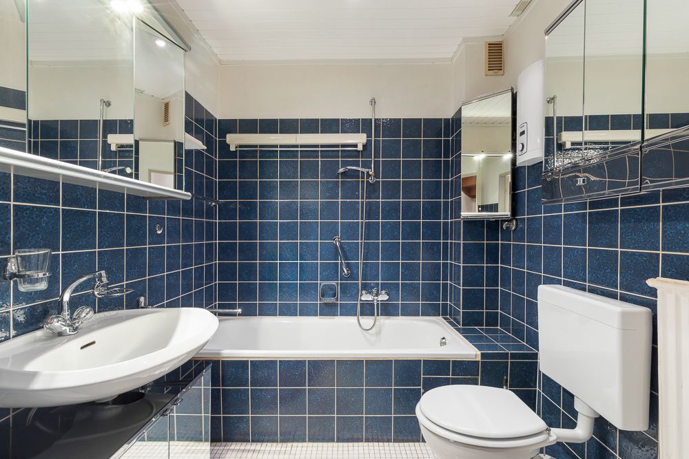 Badezimmer mit blauen Fliesen, Badewanne, Waschbecken, Spiegel und Toilette.