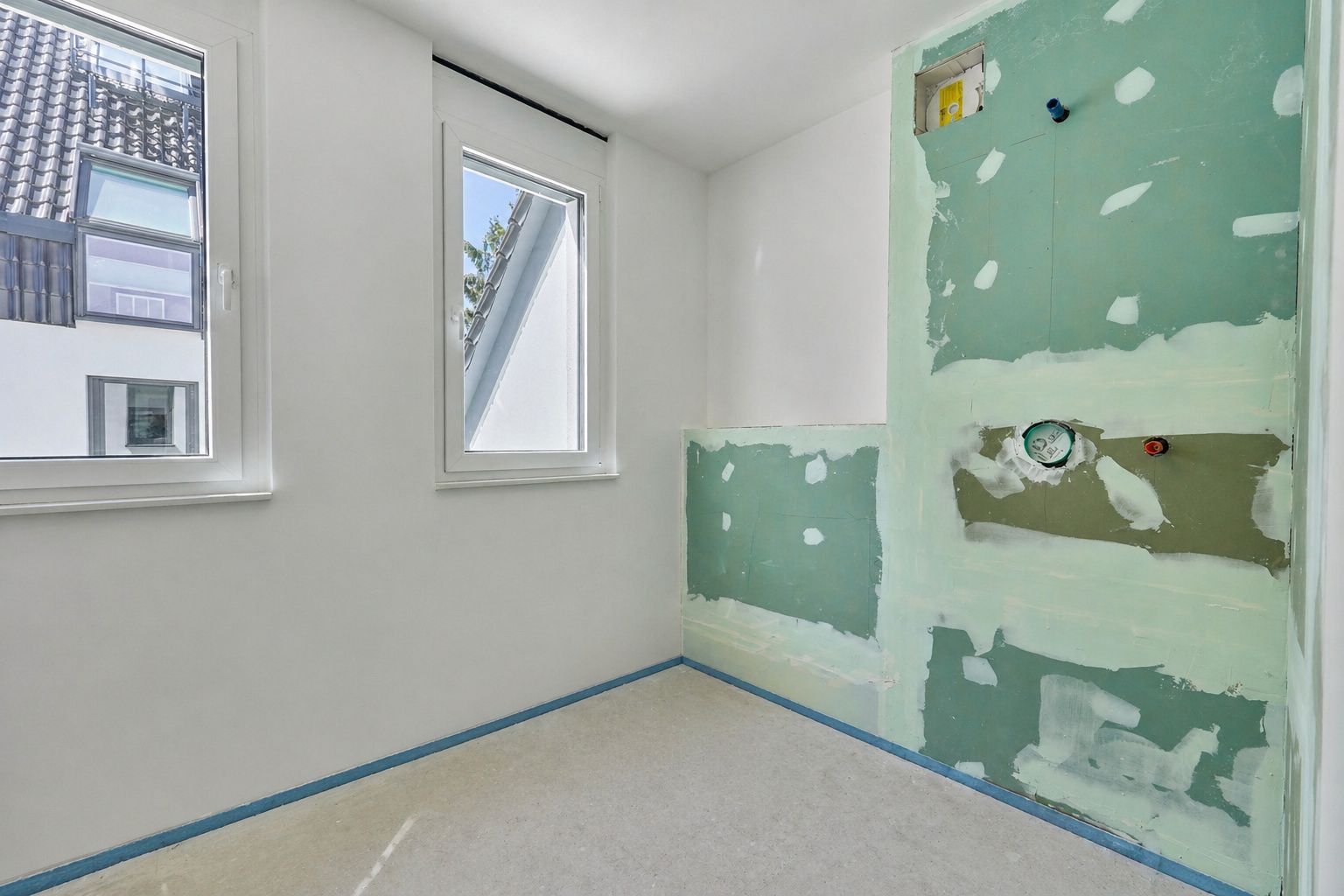 Leerer Raum mit zwei Fenstern und vorbereiteten Wänden für Sanitärinstallation.