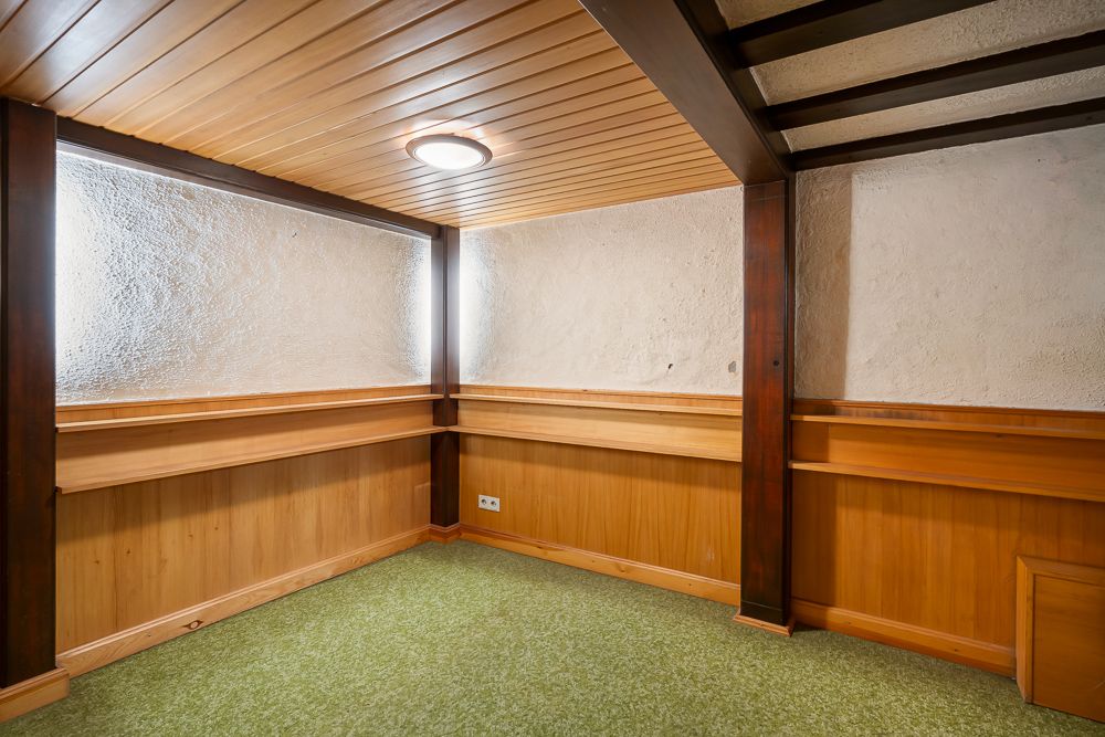 Kleiner Raum mit Holzvertäfelung, grünem Teppichboden und zwei Fenstern an der Ecke.