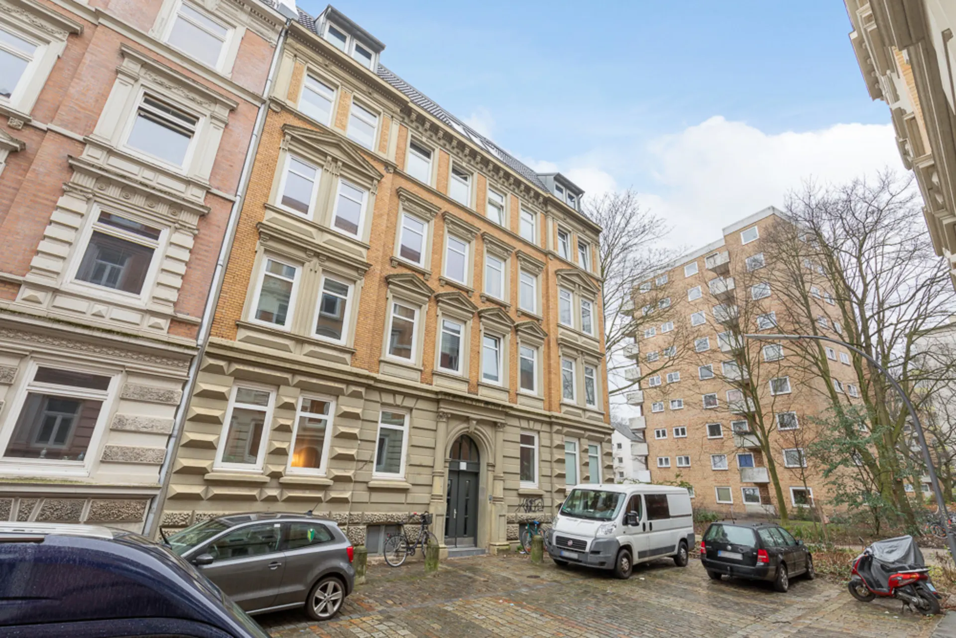 Mehrstöckiges Wohnhaus mit klassischen Fassadendetails und geparkten Autos davor.