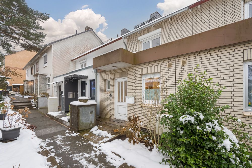 Reihenhaus mit gelben Klinkersteinen, weißer Tür und Fenstern, Gehweg, Schnee und Sträuchern im Vorgarten.