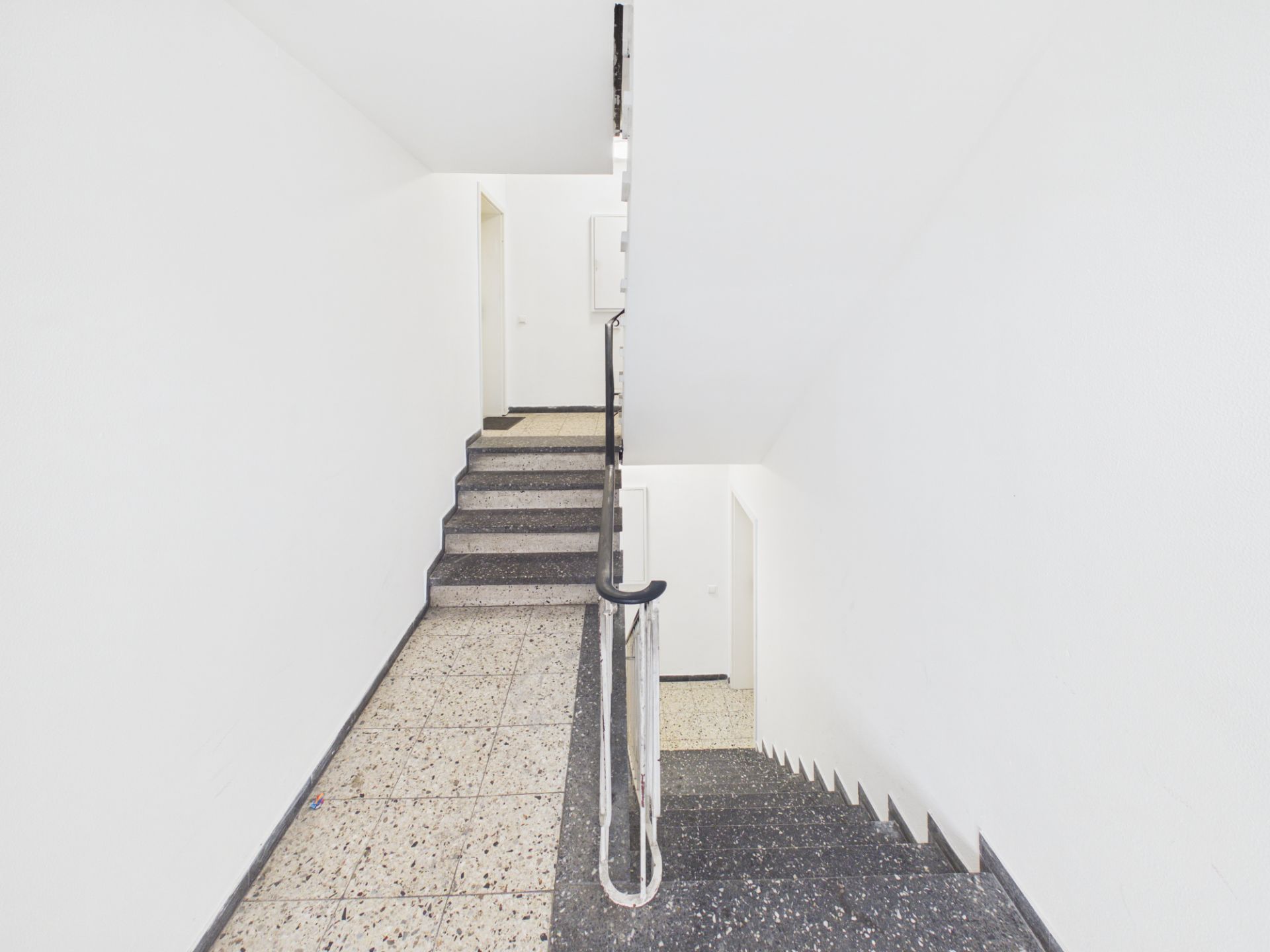 Helles Treppenhaus mit grauen Stufen und weißen Wänden in einem Wohnhaus.