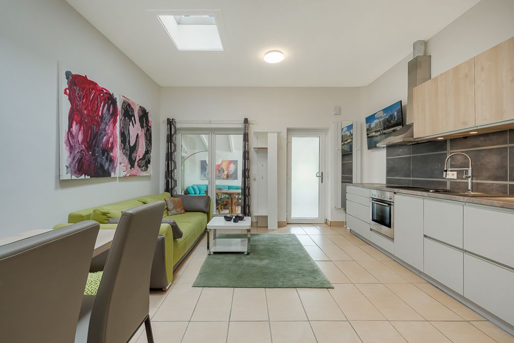 Helles Wohnzimmer mit offener Küche, grünem Sofa, Esstisch und moderner Einrichtung.
