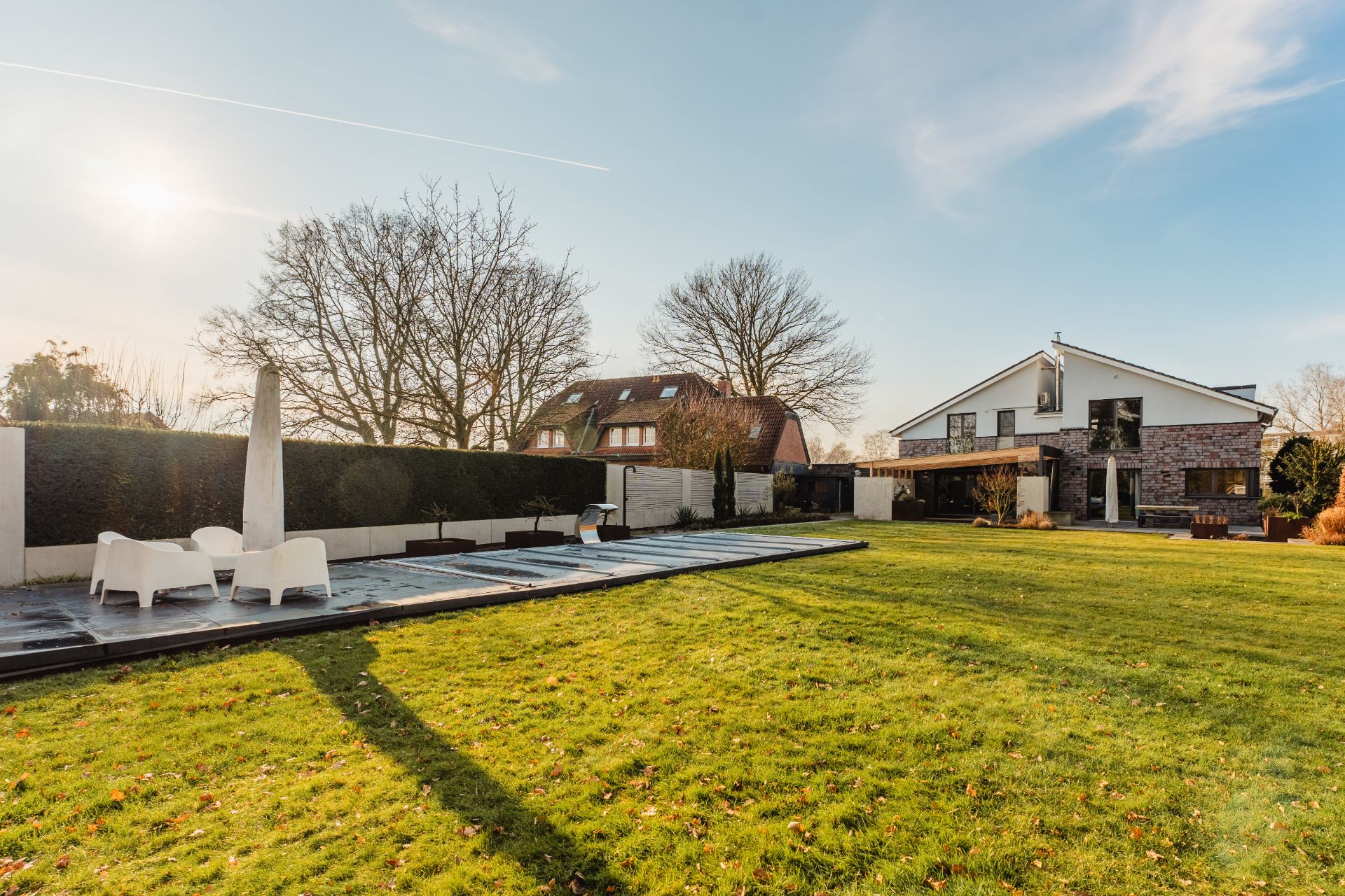 Großer Garten mit Rasen, überdachtem Pool, Sitzbereich und modernem Wohnhaus im Hintergrund.
